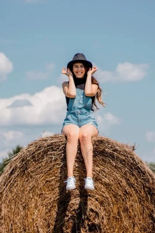 Author Laura Conaway dressed as a southern girl in overalls and sitting on a hay bale