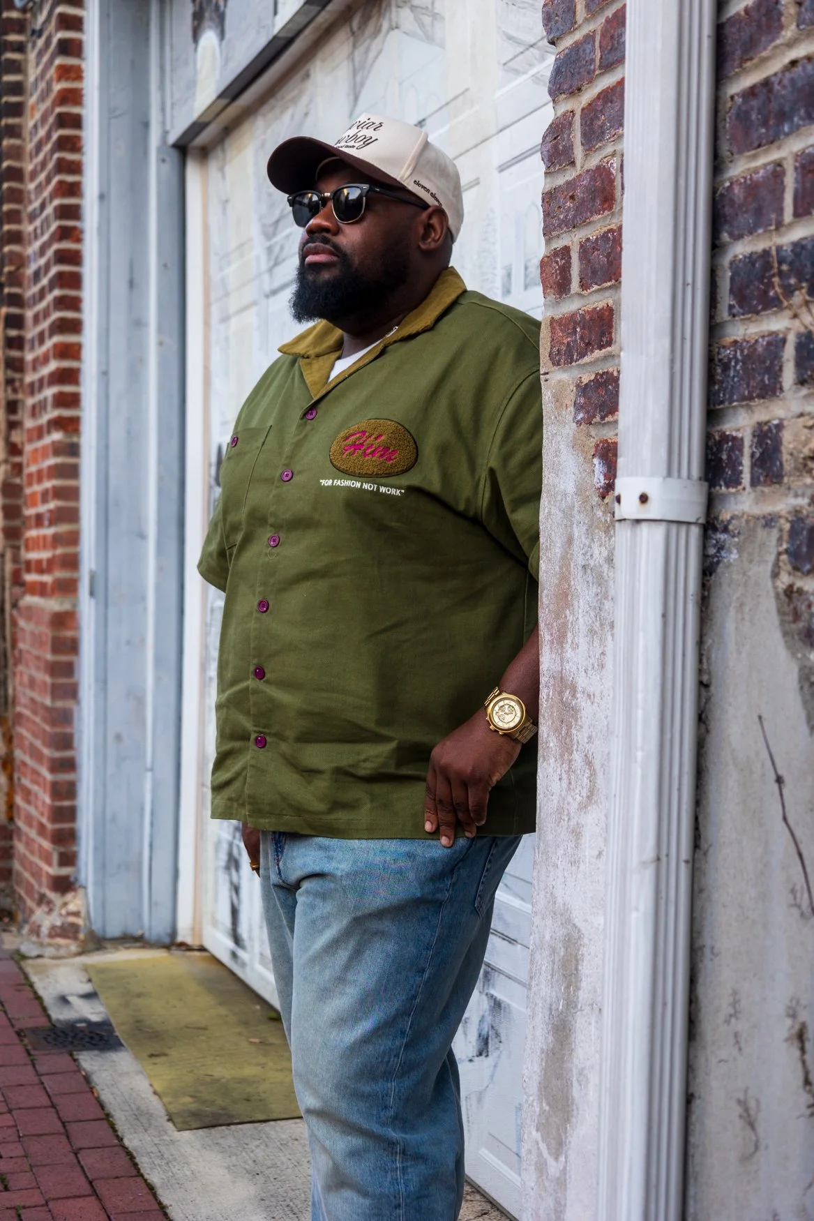 Lifestyle portrait of a man in sunglasses posing beside a brick building.