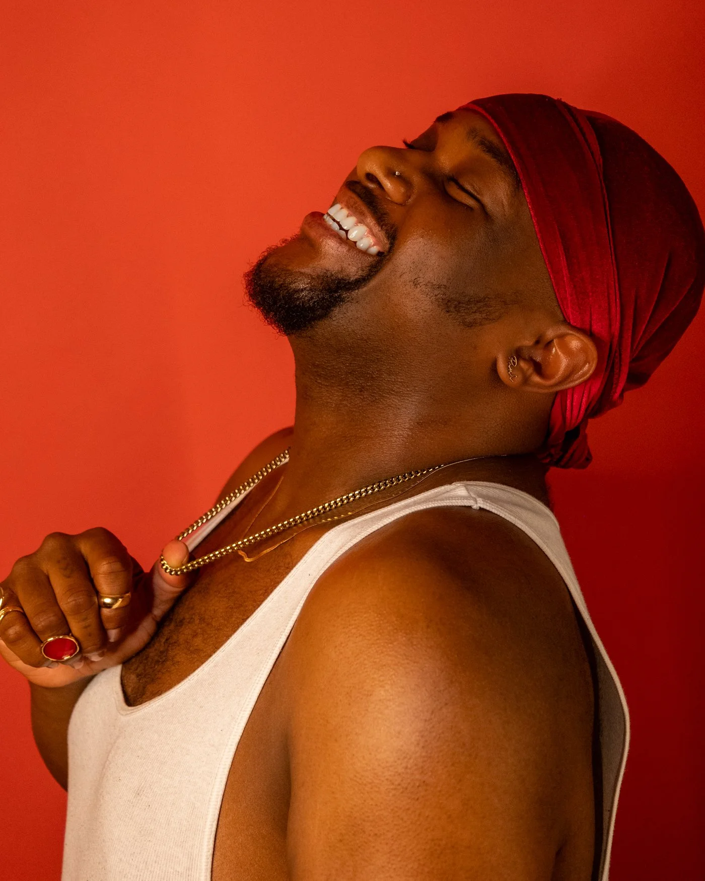 Creative studio portrait of a smiling man in a red headwrap against a warm red background.