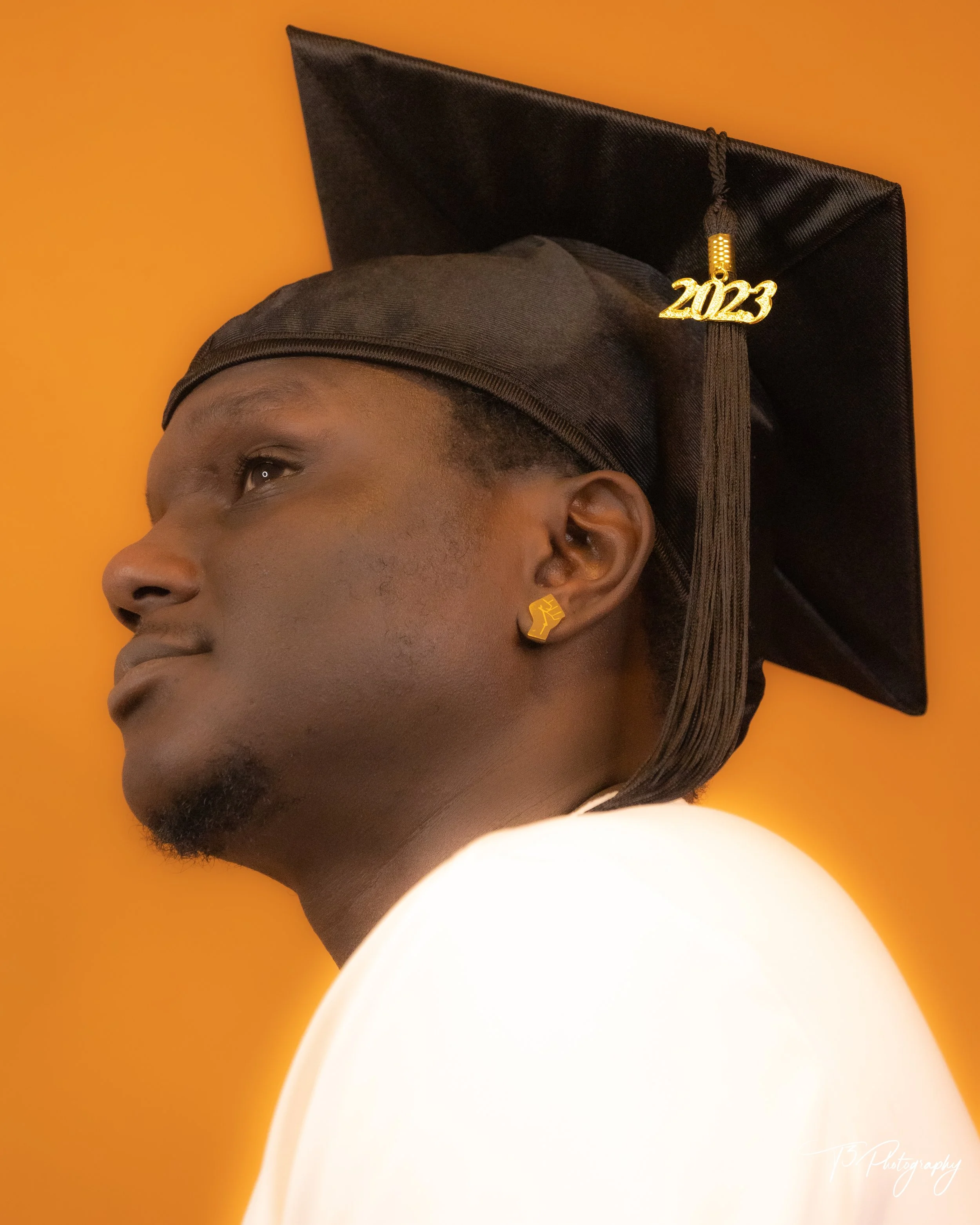 Graduation portrait of a man in his cap and gown against a warm orange background.