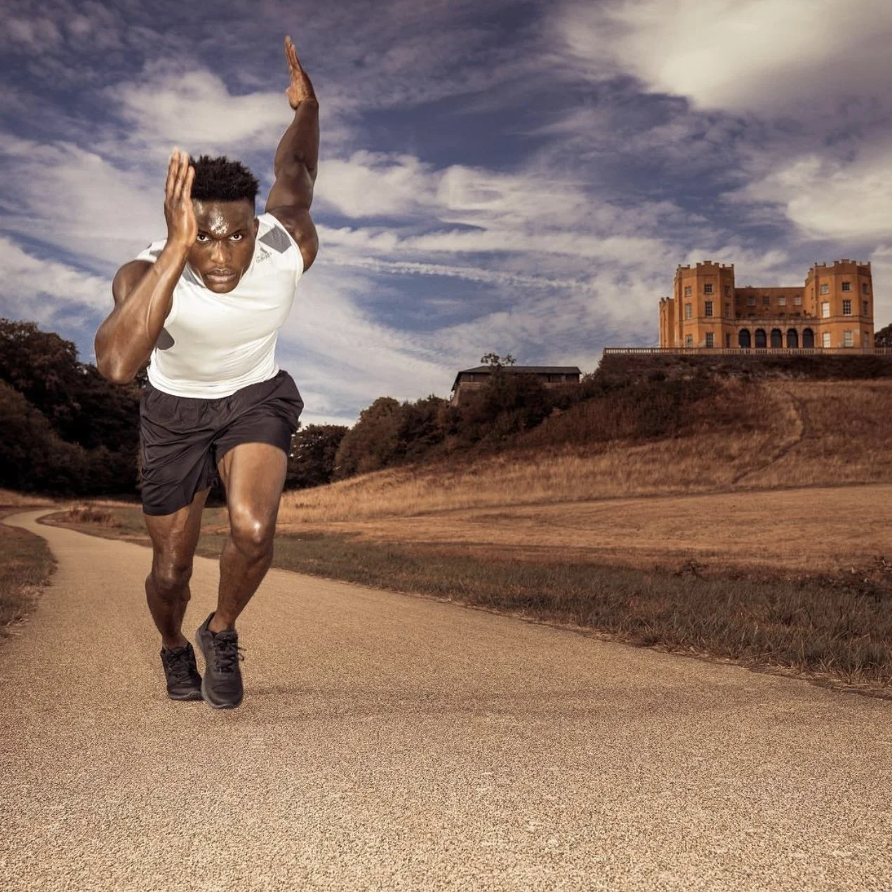 Athlete sprinting outdoors on a paved path with a historic building in background, under a cloudy sky.