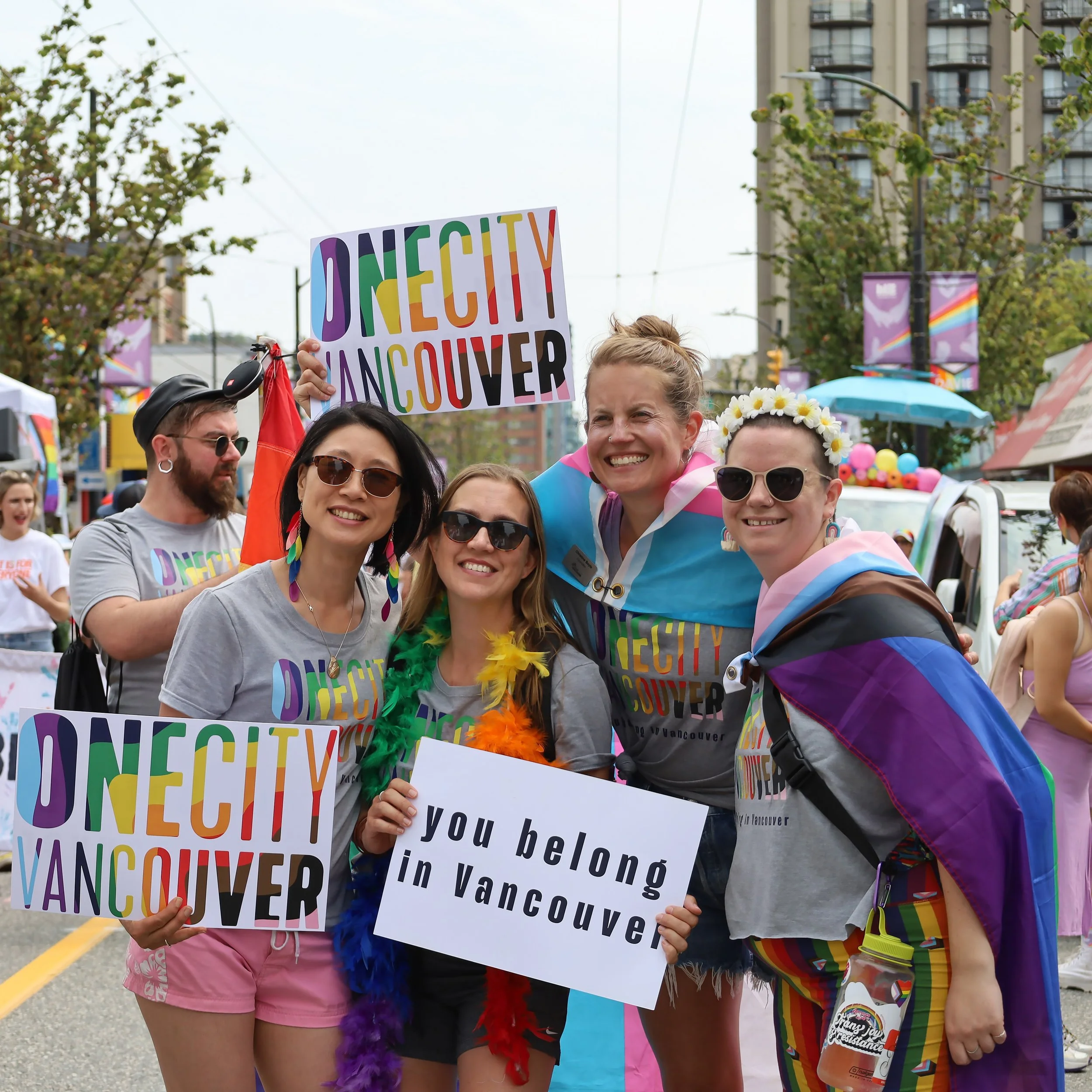 Image of Iona Bonamis attending the Vancouver Pride Parade with other OneCity members, holding OneCity Vancouver and "You belong in Vancouver" signs.