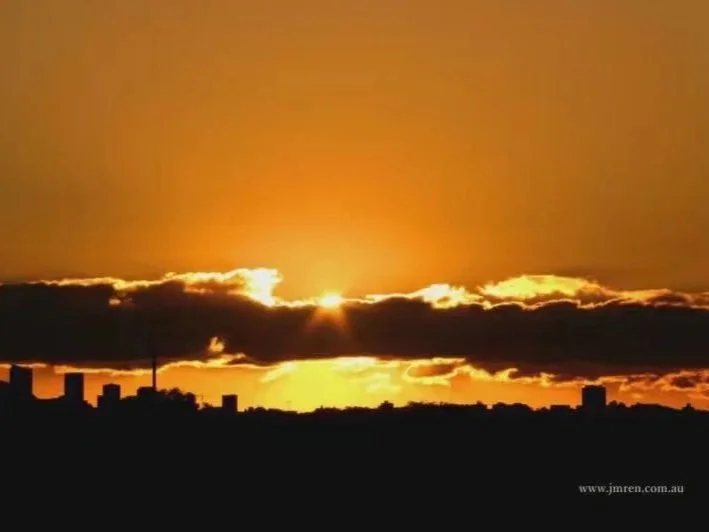 Golden sunrise appearing above clouds and the Sydney skyline, photographed by Jingmin Ren.