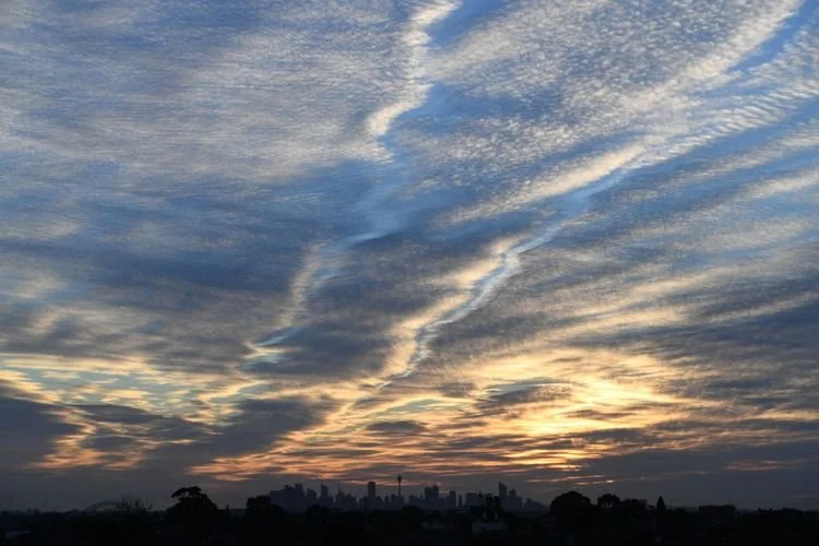 Layered cloud formations illuminated by changing morning light over Sydney, photographed by Jingmin Ren.