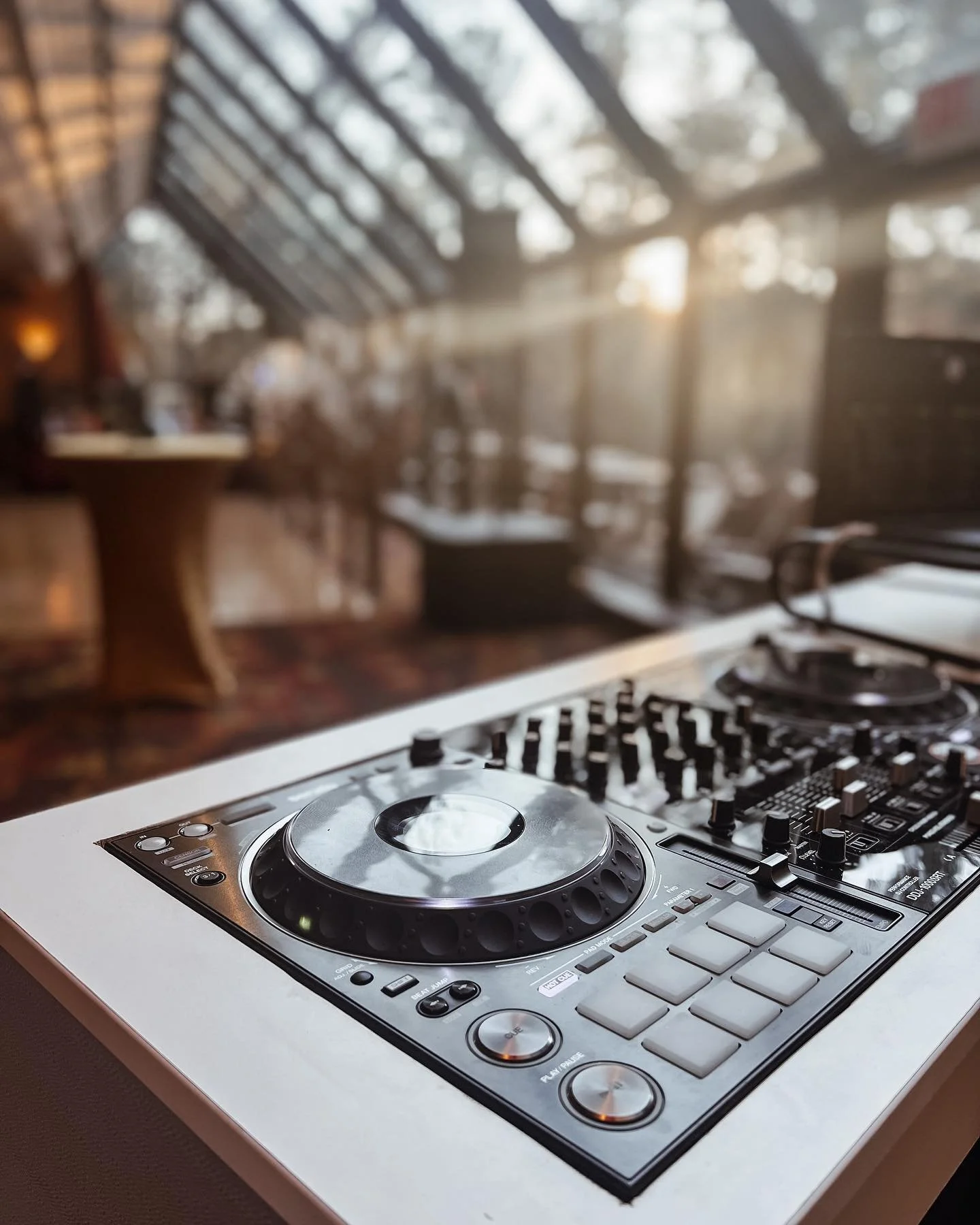 DJ turntable and mixer with large window and sunlight in the background.