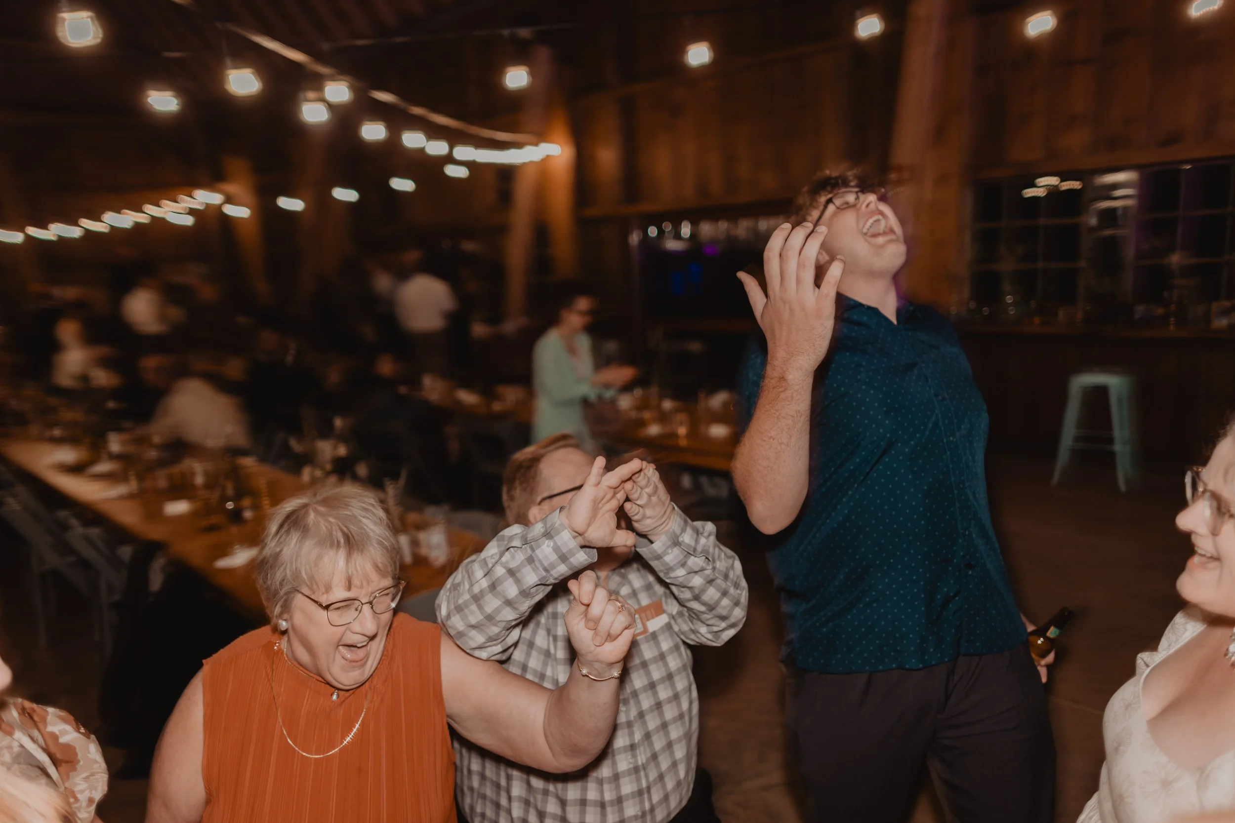 People dancing and enjoying themselves at a lively indoor celebration or party with string lights overhead.