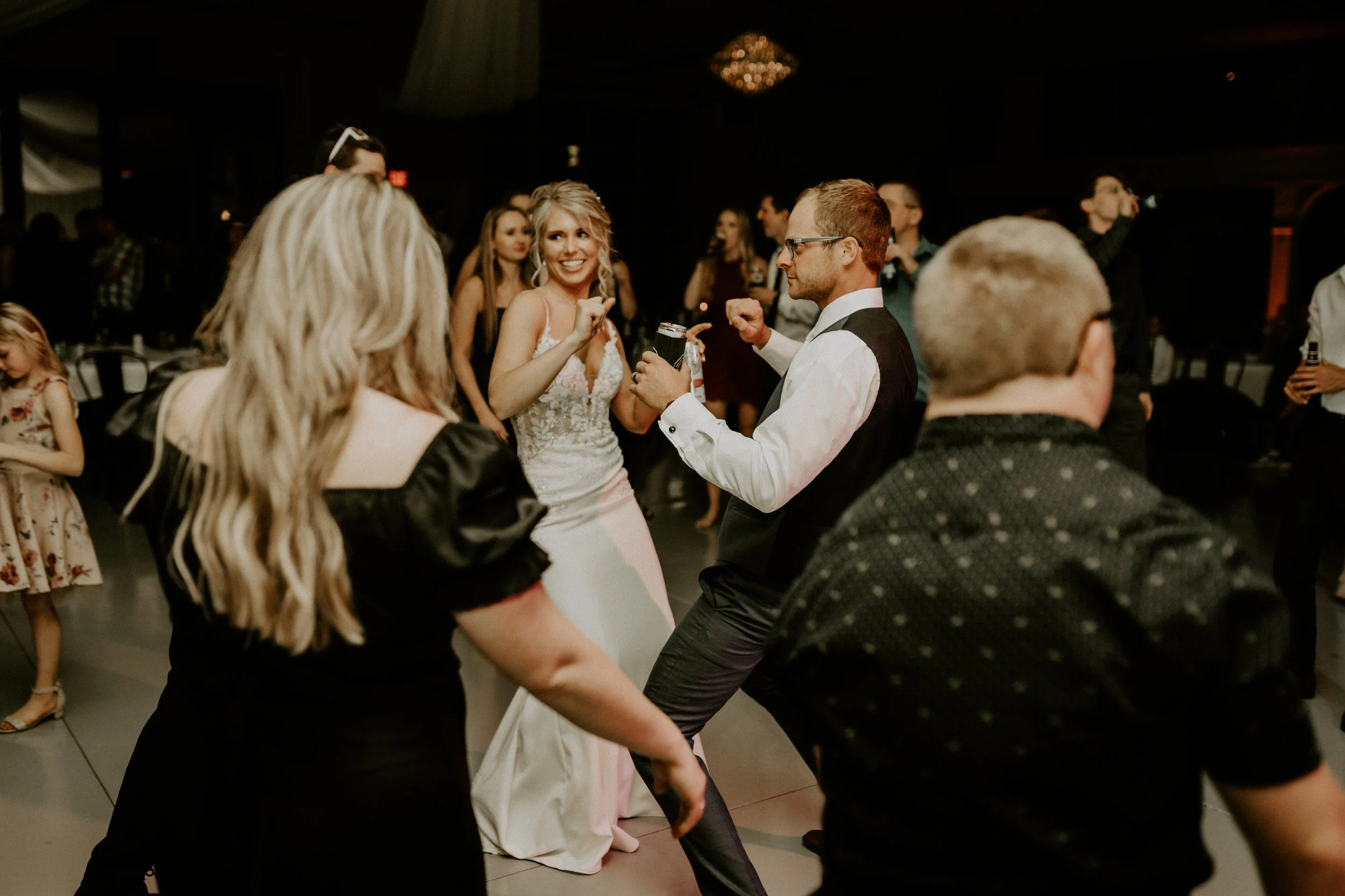 People dancing at a wedding reception, with the bride smiling and holding a drink.