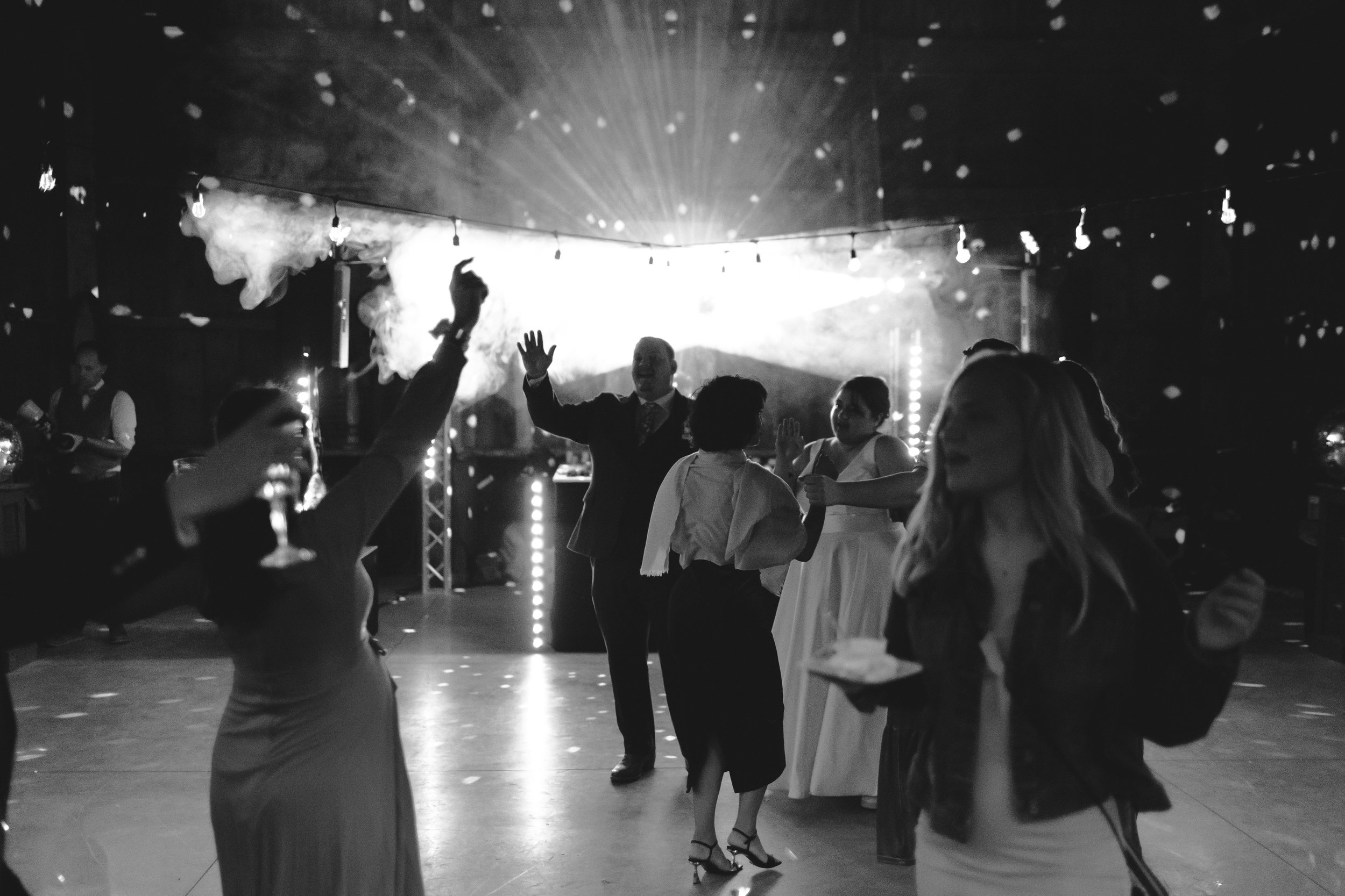People dancing and socializing at a celebration or party with lights and fog effects.