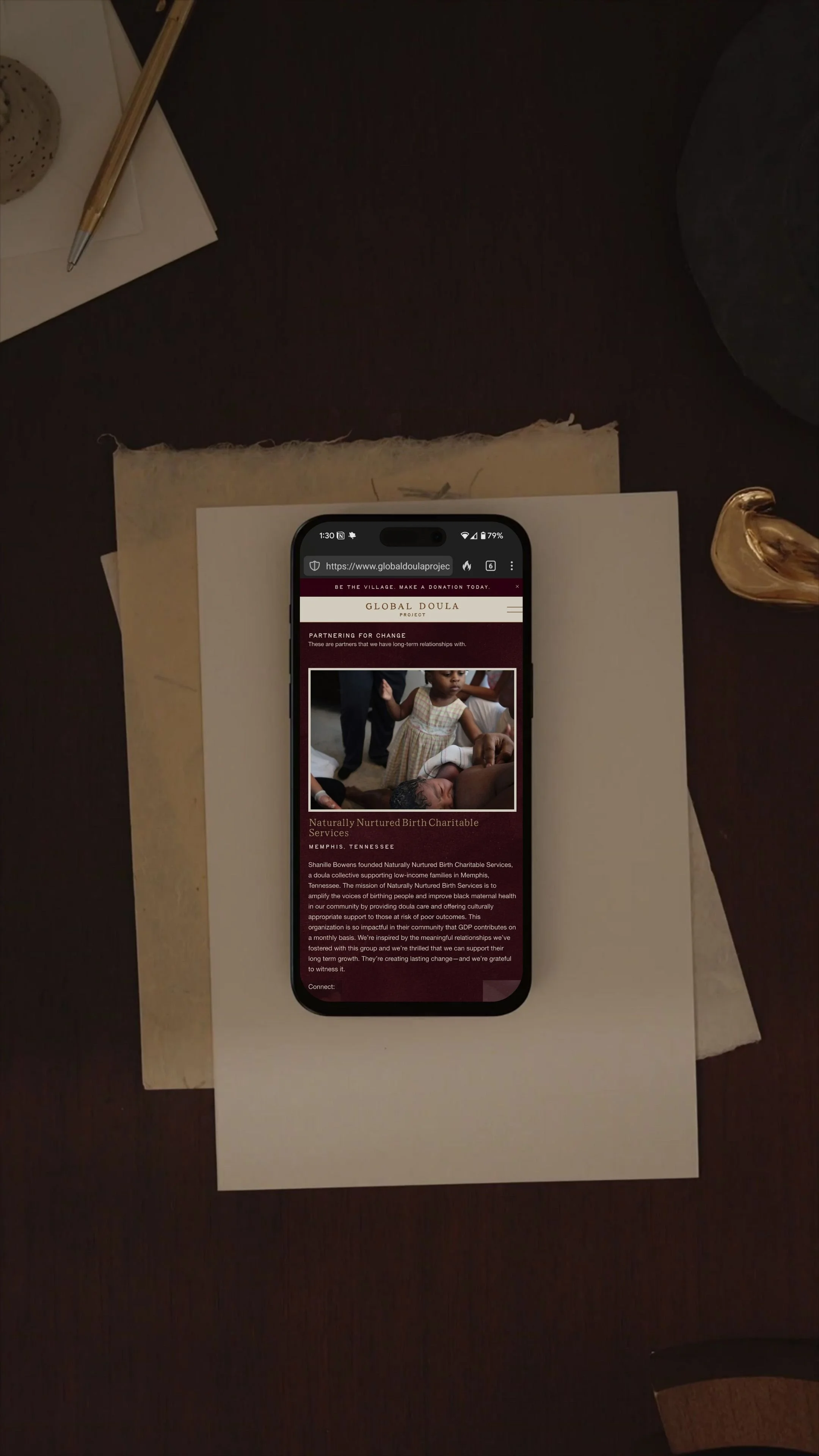 Smartphone on desk with website open, surrounded by paper and pen