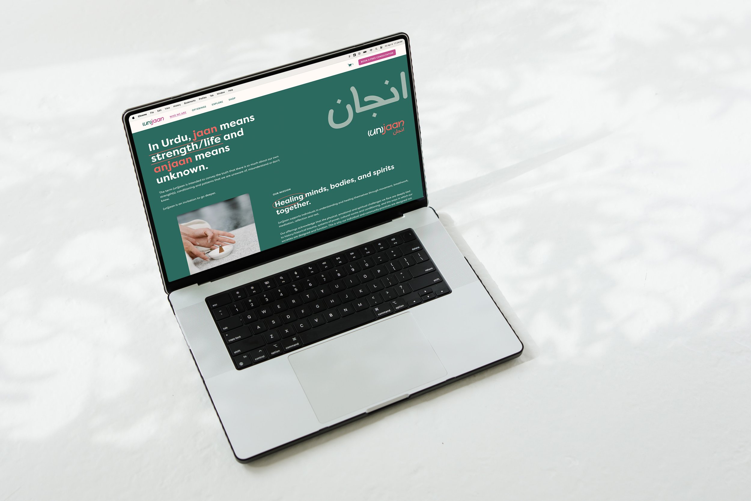 Open laptop on white surface displaying a website about the meaning of 'unjaan', a word meaning strength, life, and the unknown in Urdu, with text and an image of a hand holding a white stone.