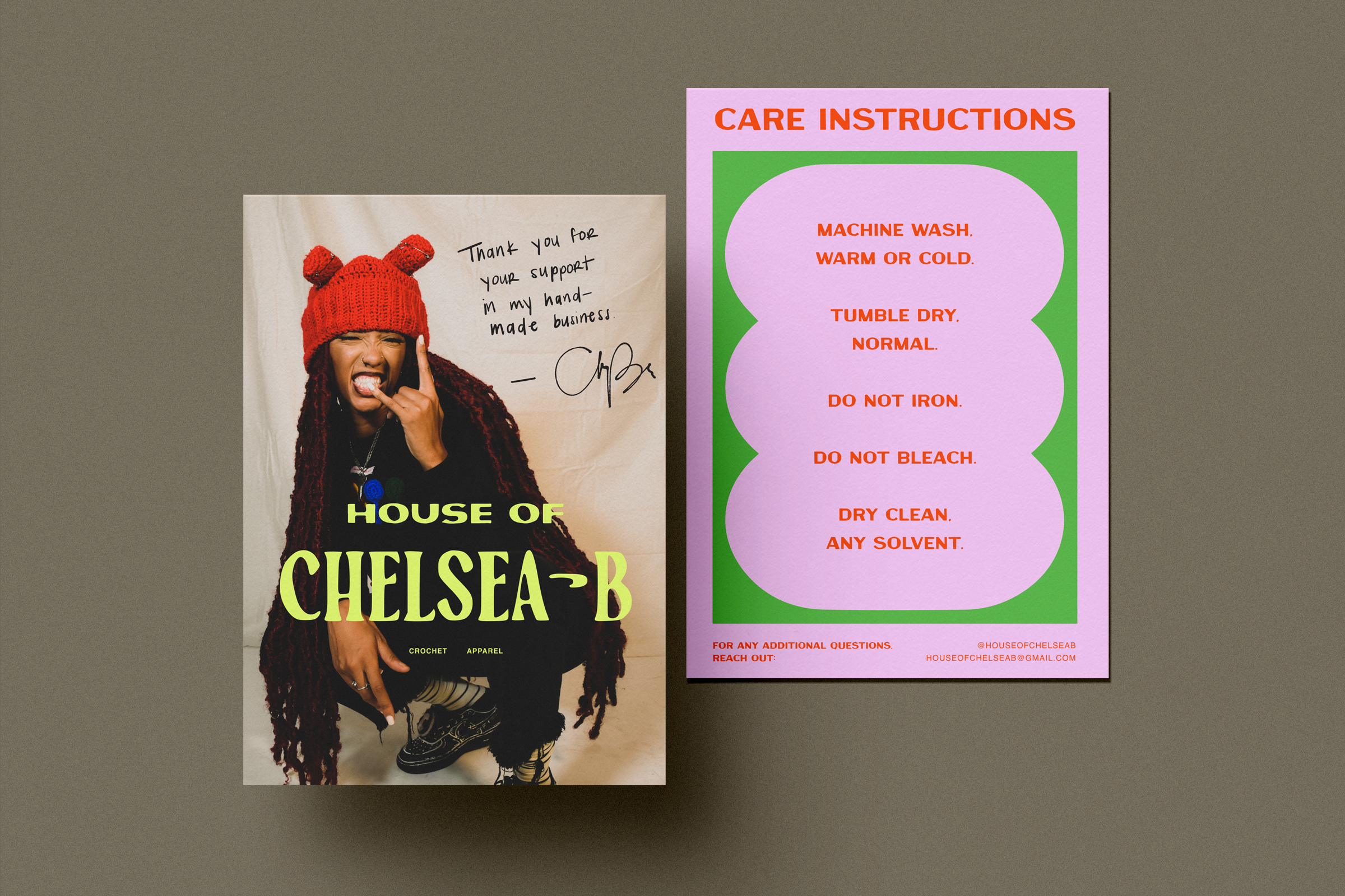 Close-up of a handmade crochet product care instruction sheet with steps in bold red text on a purple and green background, and a partial view of a magazine cover featuring a woman with long red braids, wearing a red knit hat with pom-poms, making a playful face with her tongue out and hand near her face, and holding a sign with a supportive message.