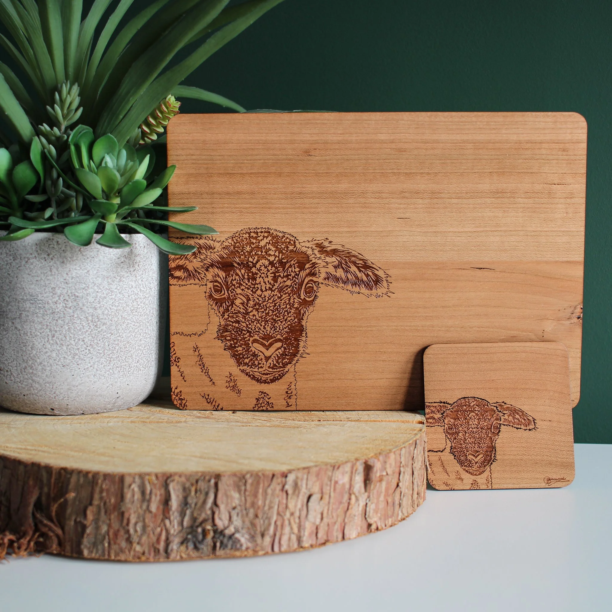 Wooden lamb placemat and coaster displayed upright against a plant pot on a log slice against a dark green backdrop.