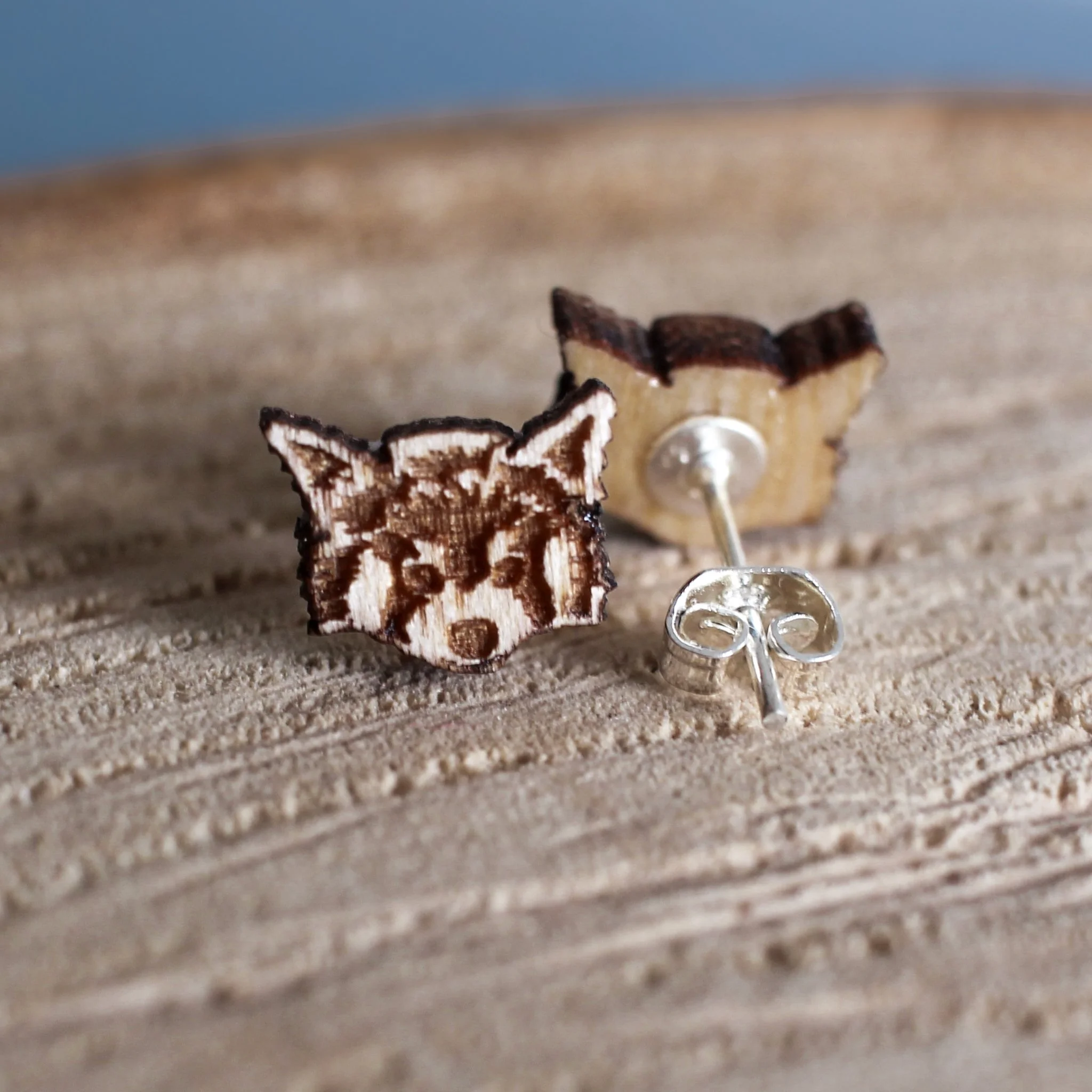 Wooden stud earrings on a log slice. One earring faces outward showing a detailed red panda engraving. The other is reversed showing a silver post back with butterfly fastening resin set to the wood.