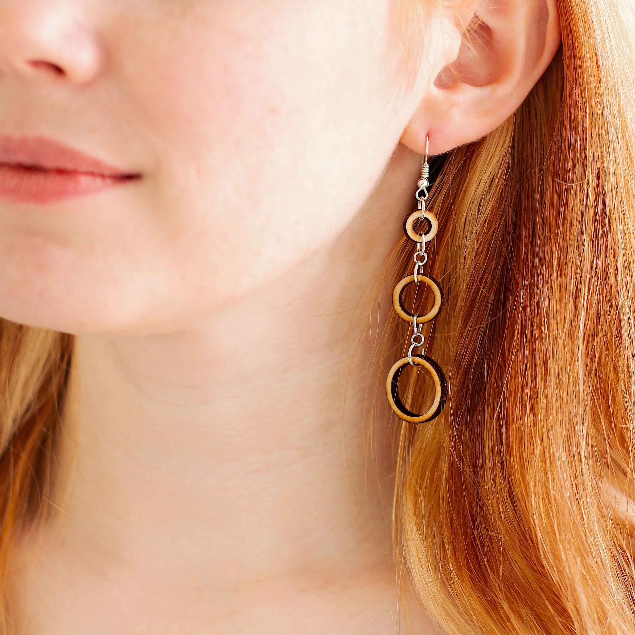Woman wearing dangly earrings made from wood circle hoops and silver pieces.