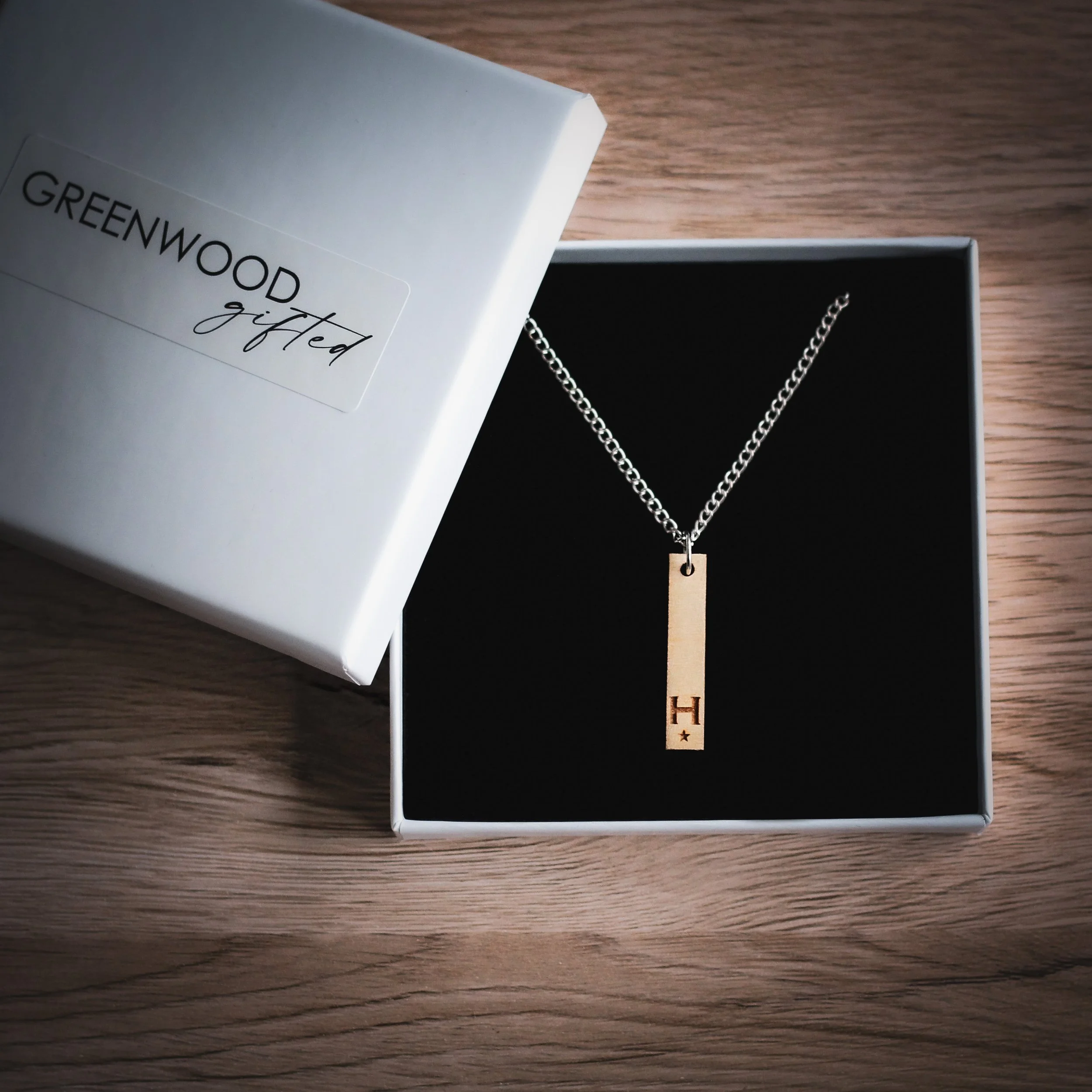 Personalised necklace in a gift box. The gift box is square and white and the necklace sits on a black pillow inside.