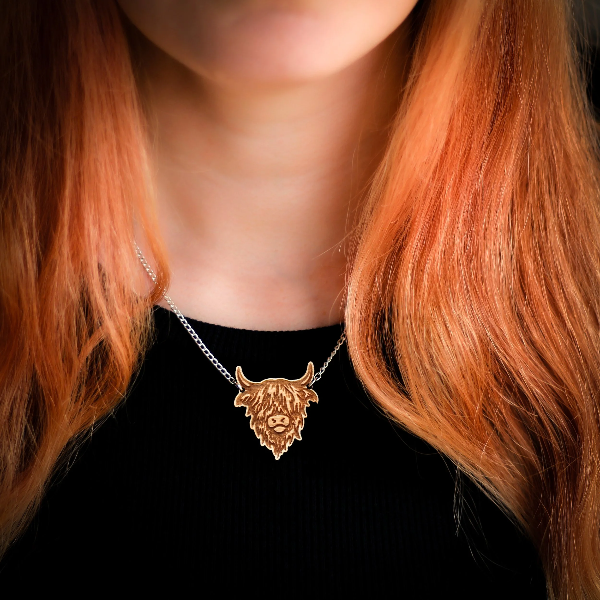 Woman wearing wooden highland cow pendant. The pendant is linked at the base of the cow’s horns to a silver chain which attaches around the wearer's neck.