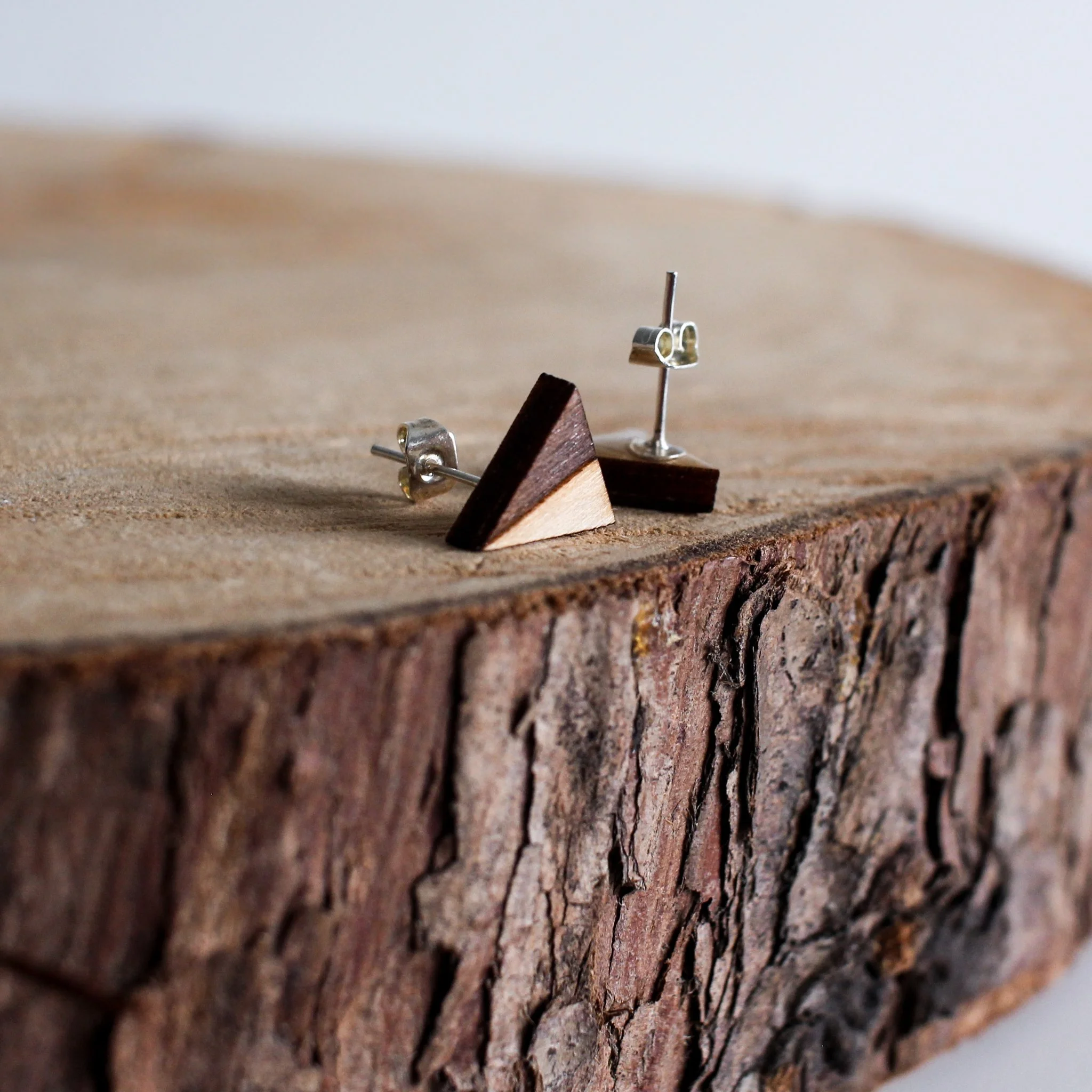 Detail shot of a pair of wooden stud earrings with a resin set silver plated post back and butterfly scroll fastening.