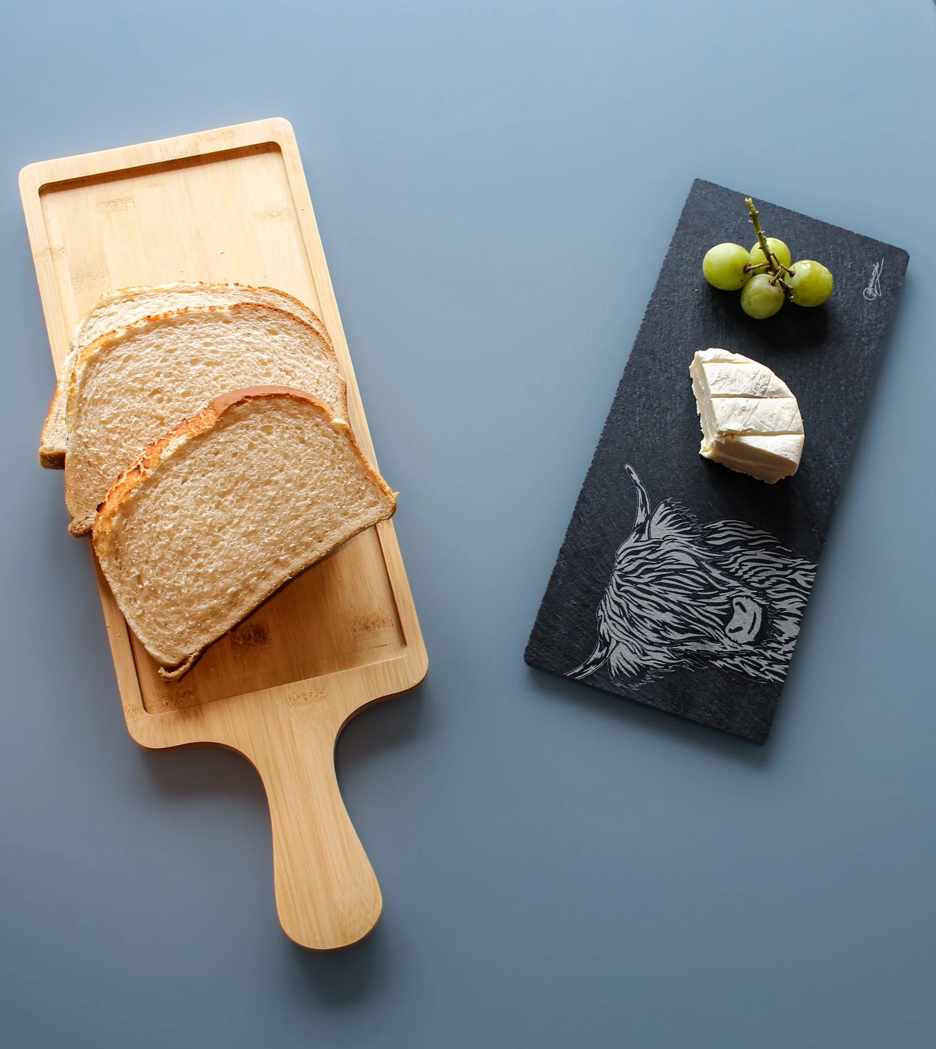The highland cow serving platter in use in two separate parts: the bamboo tray is on the left serving bread, separately on the right the slate tray is removed and holds cheese and grapes.