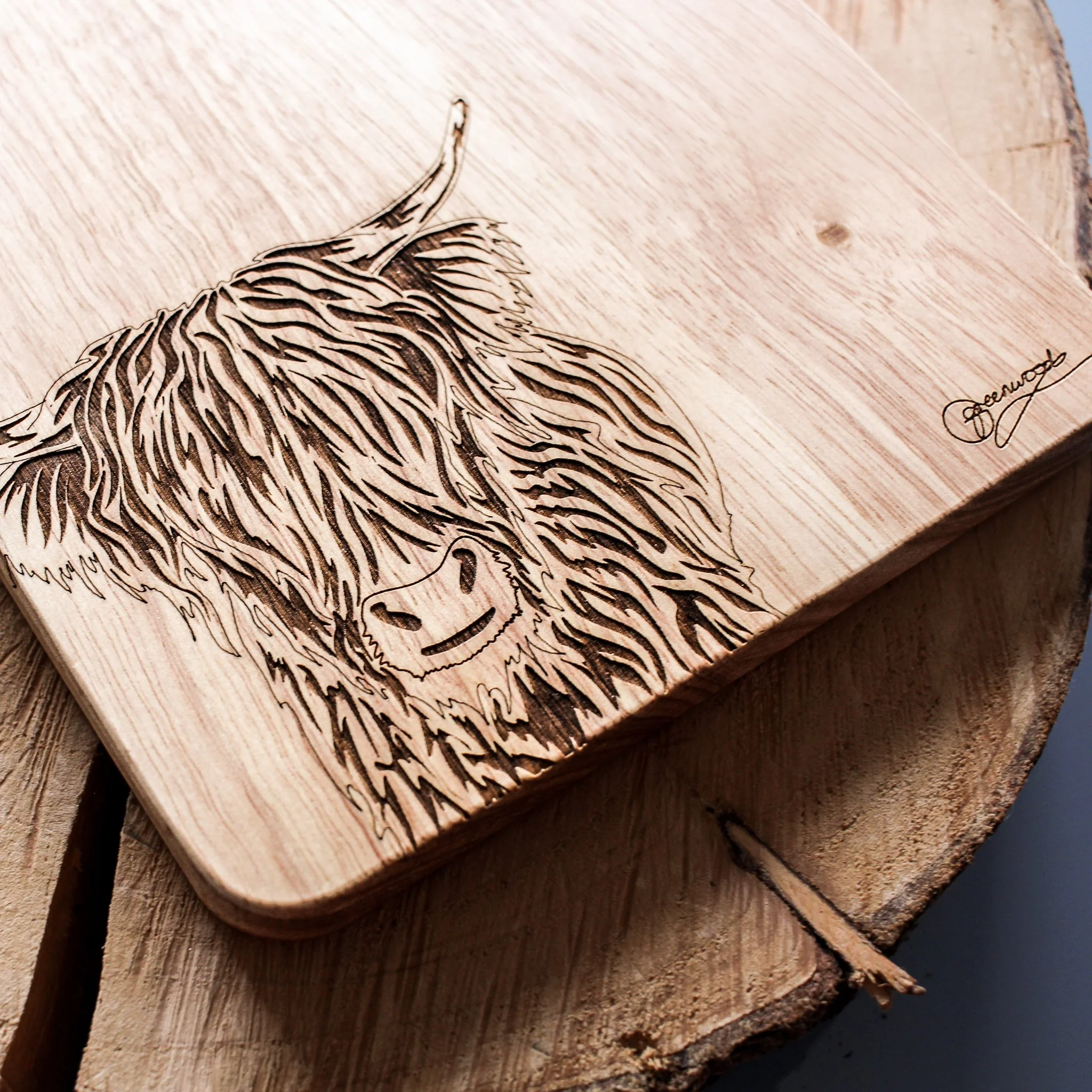 Detail shot of highland cow art engraving on wooden chopping board. The shaggy darkened texture sits slightly indented in the woods surface. The artists signature has also been engraved.