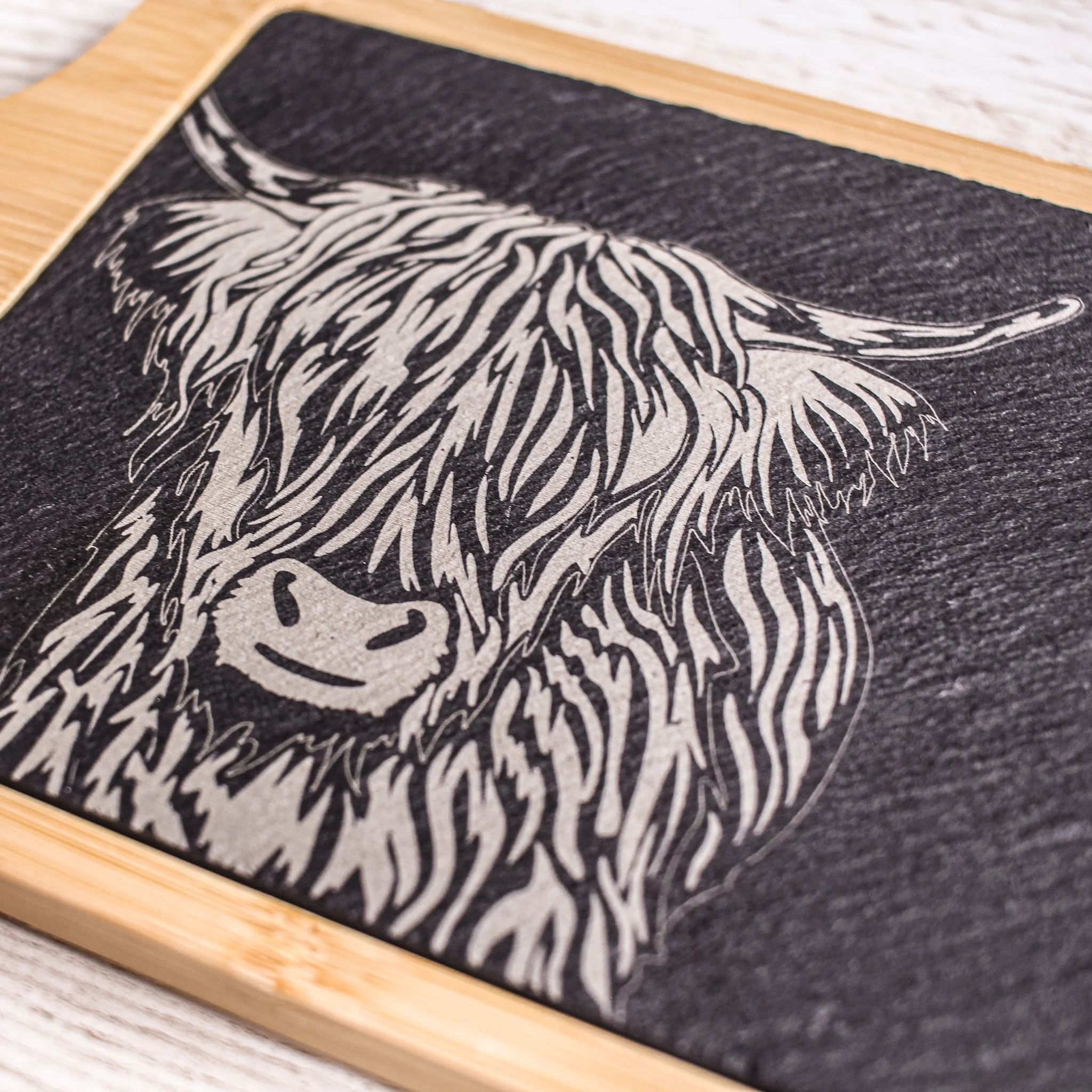 Detail shot of hand drawn highland cow illustration laser engraved onto slate, set into bamboo tray.