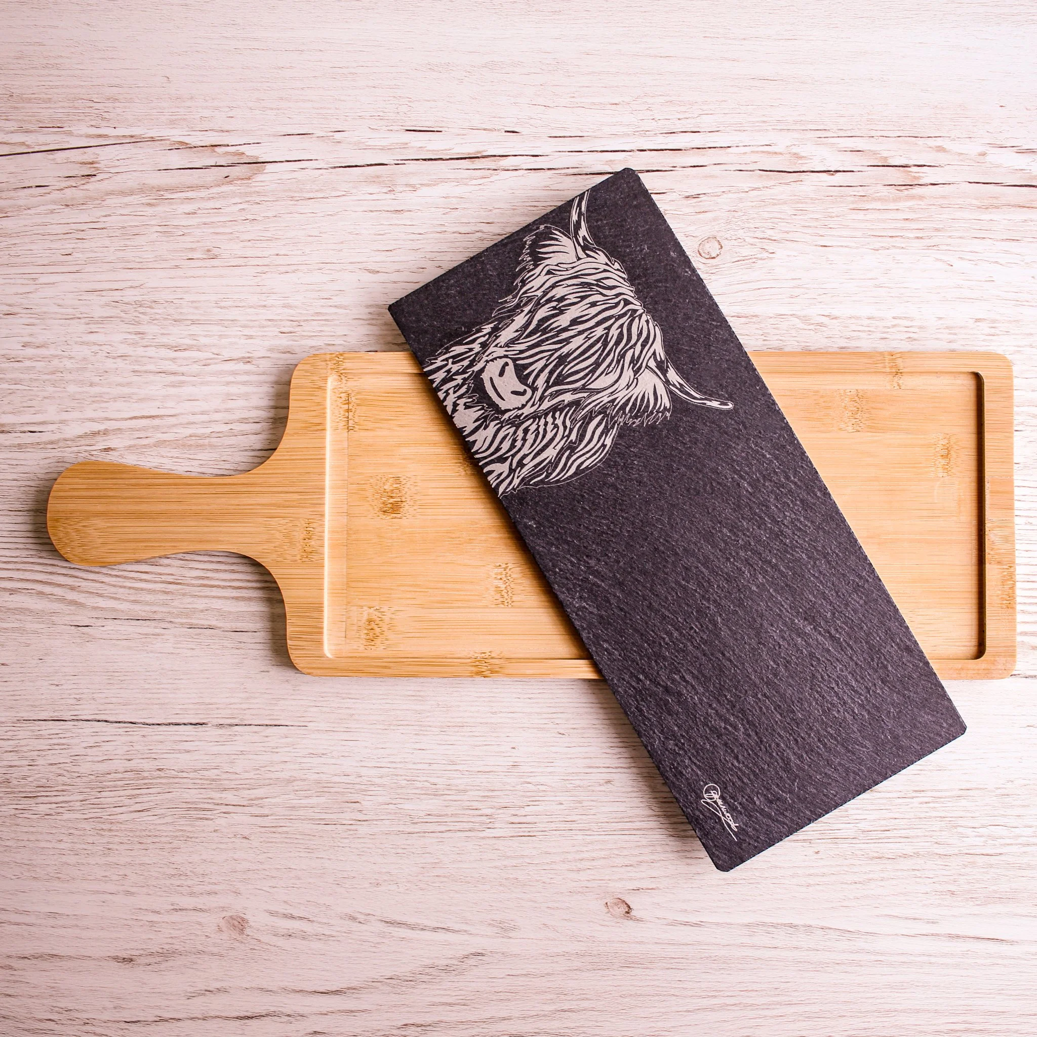 Highland cow serving platter. Image shows slate insert removed from the bamboo tray and placed at an angle on top of the warm wooden piece.