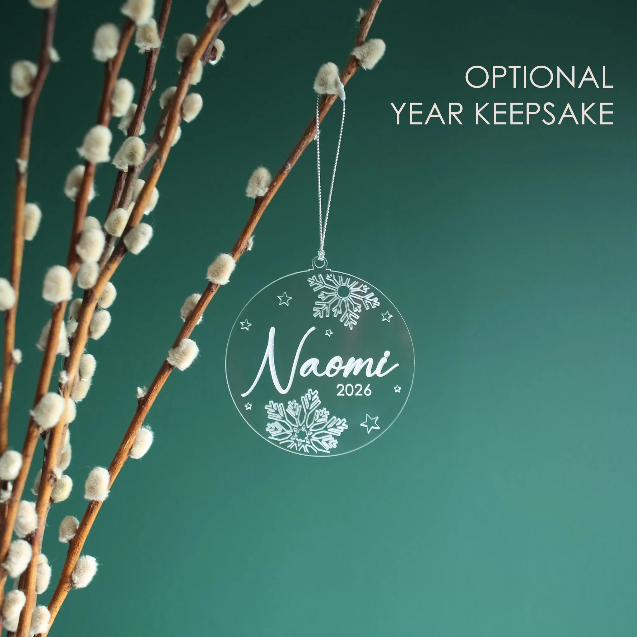 Personalised clear acrylic Christmas ornament with the name and year, Naomi and 2026, engraved with snowflakes and stars and hand-painted in white.