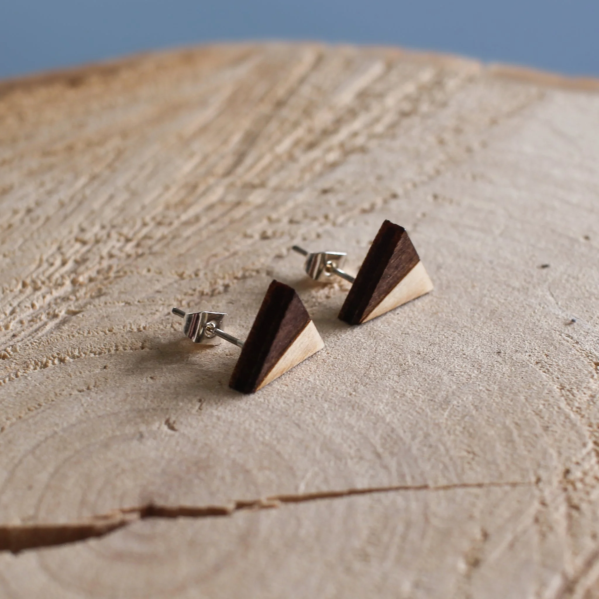 Two tone geometric earrings displayed on a log slice. The earrings are made from wood and have a silver post and back.