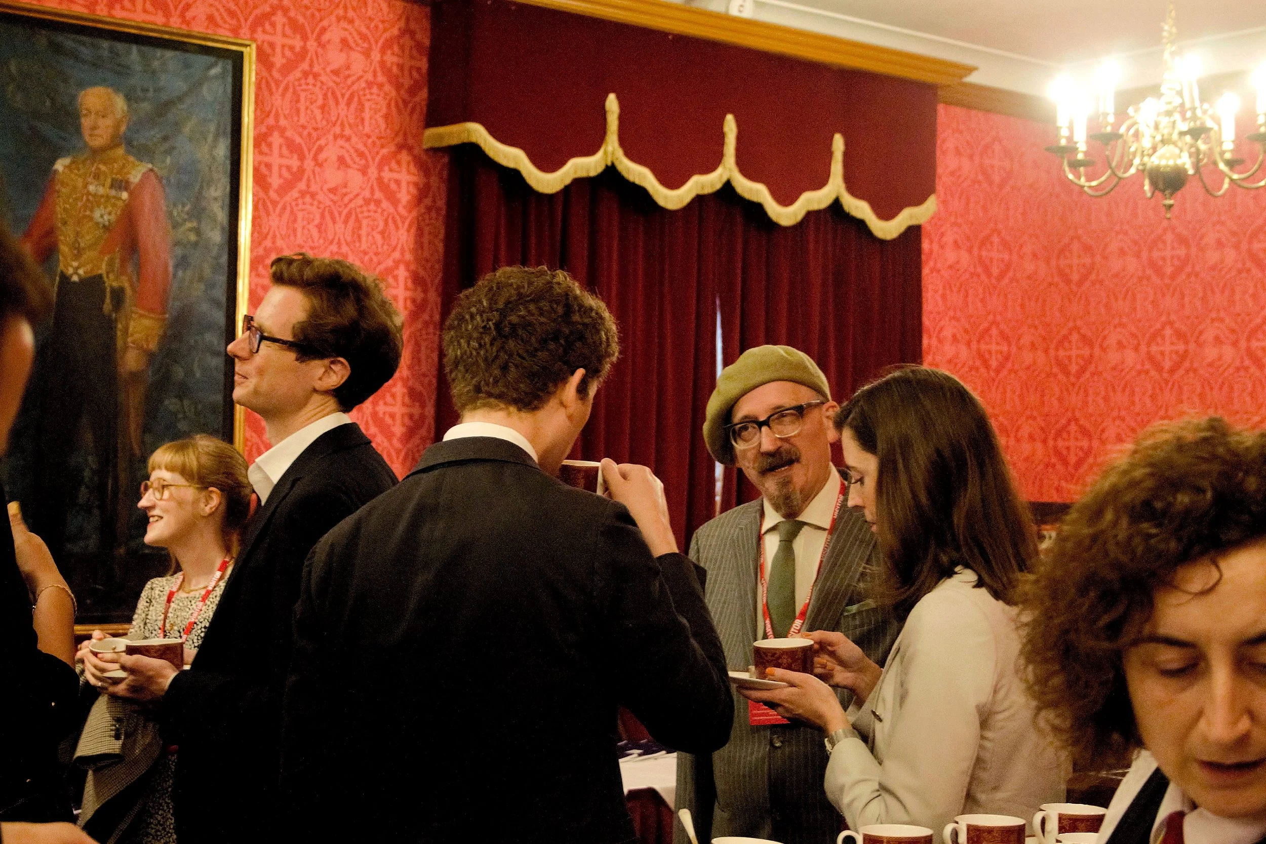 Wide shot of guests conversating in the red room, three of the guests are togther in one conversation, there is a red curtain in the background and a portrait