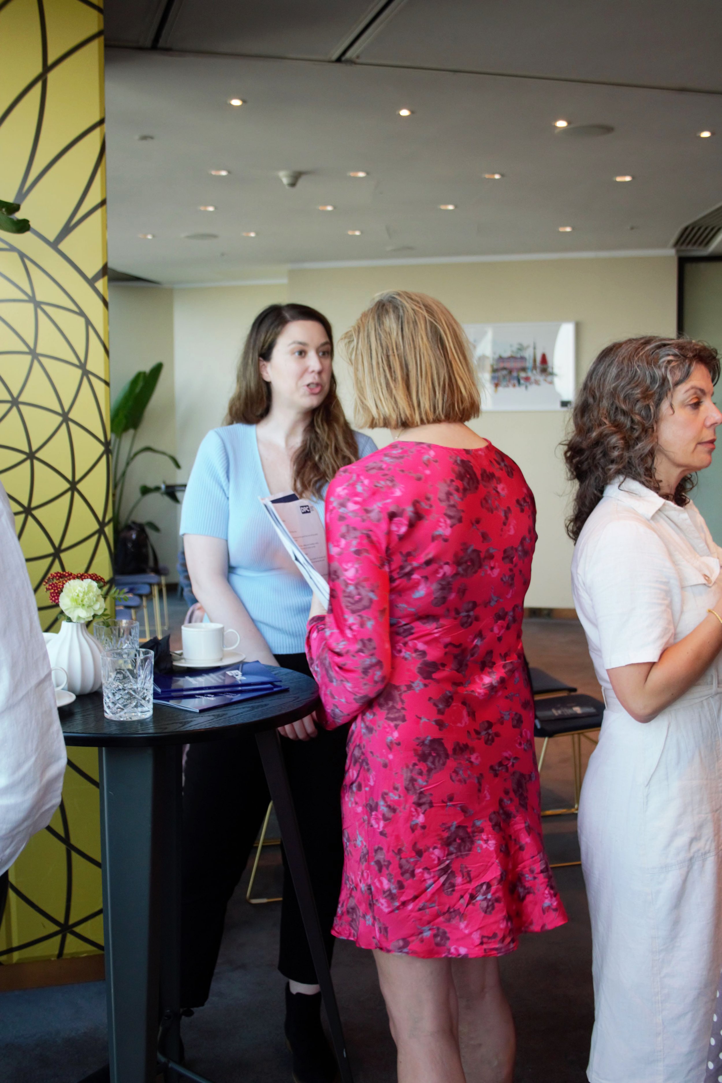 Photograph of the back of Alys speaking to another lady stood infront of her. She is in a pink floral dress.