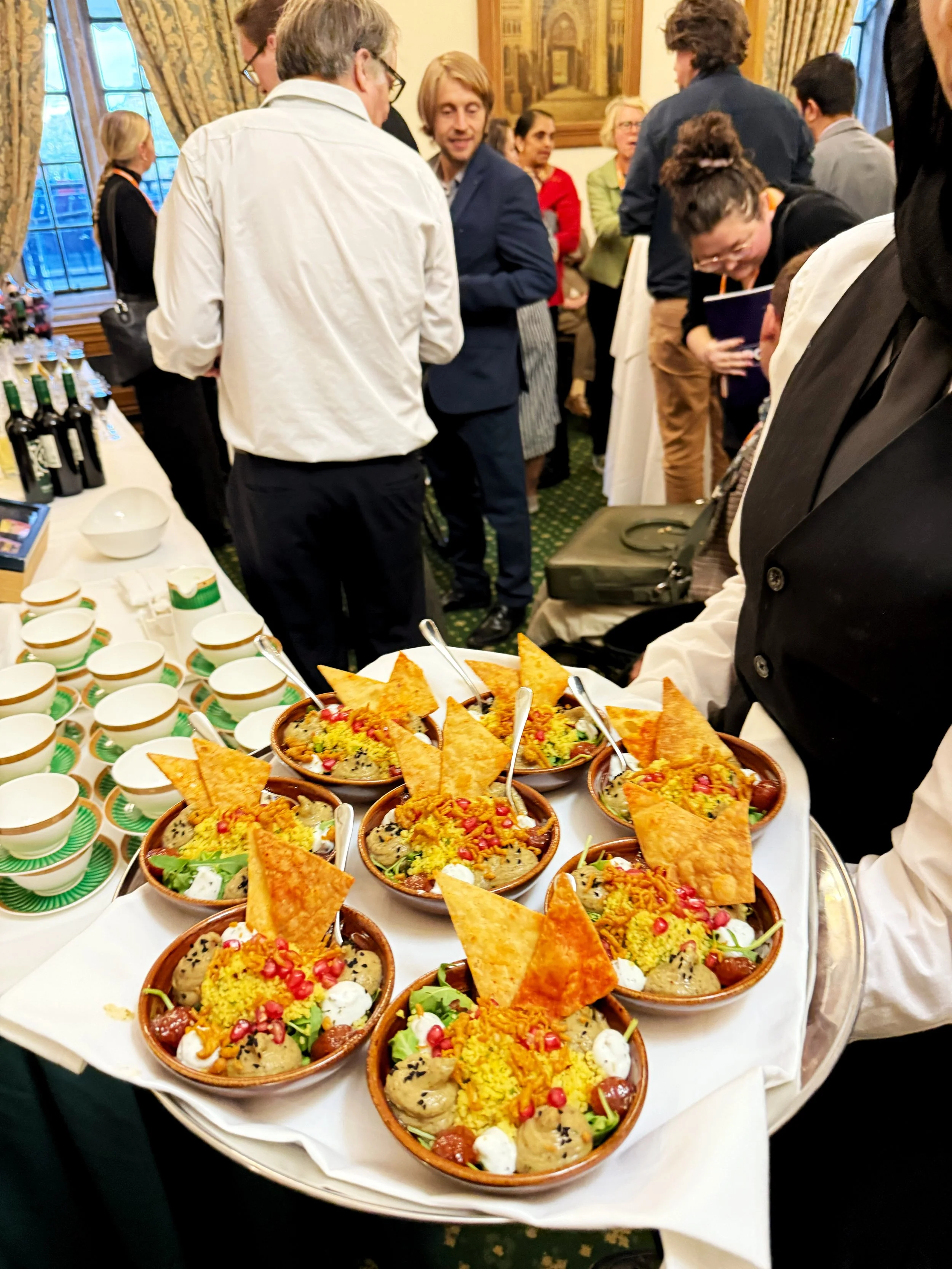 A photograph of the Churchill Room in the Houses of Parliament featuring a waiter holding up a tray of appetisers. In the background guests can be seen mingling.