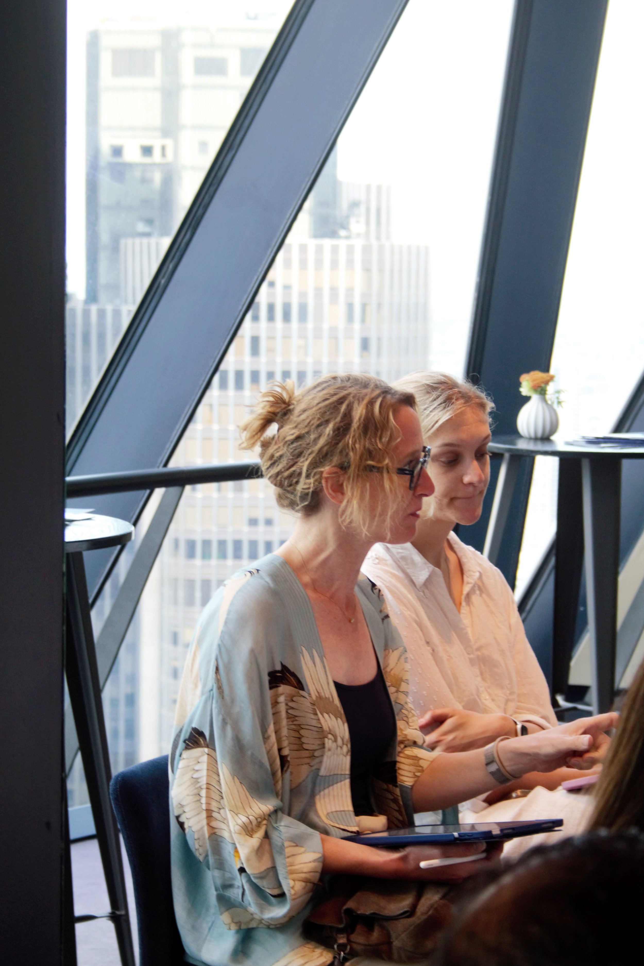 Photograph of a female audience member engaging with the crowd. She in front of a large window overlooking London. She is wearing a light blue asian kimono with a black tank top underneath.