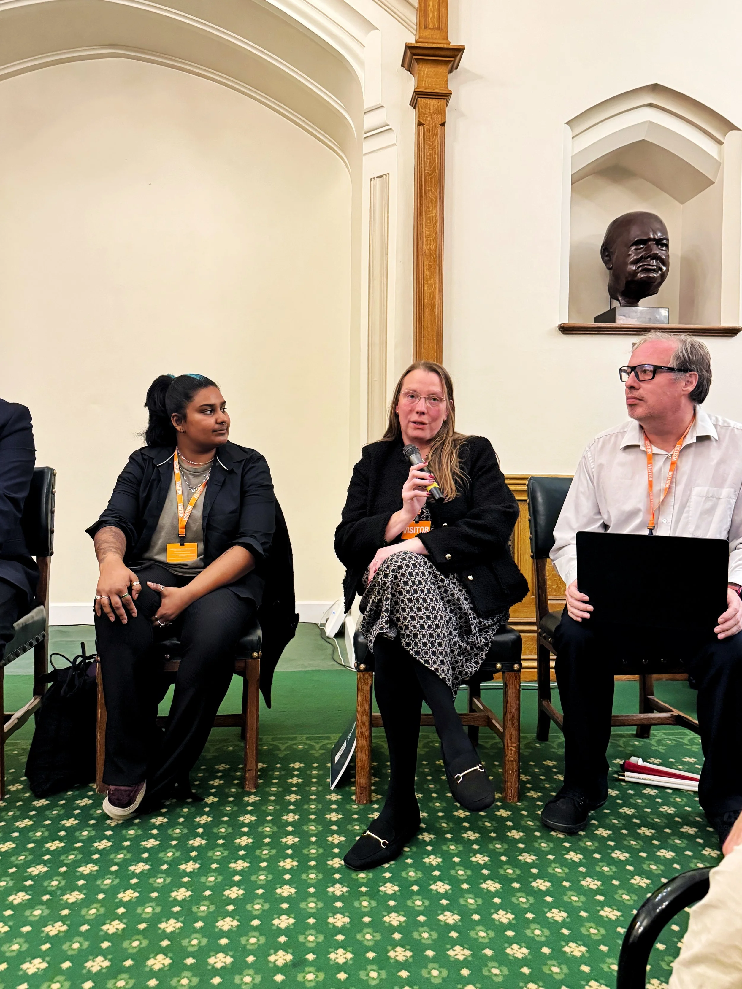 Panel session in the Churchill Room, Houses of Parliament, with Ria Patel seated beside Michelle Anglesea, who is speaking into a microphone, and Mike Wordingham holding a laptop on his lap.