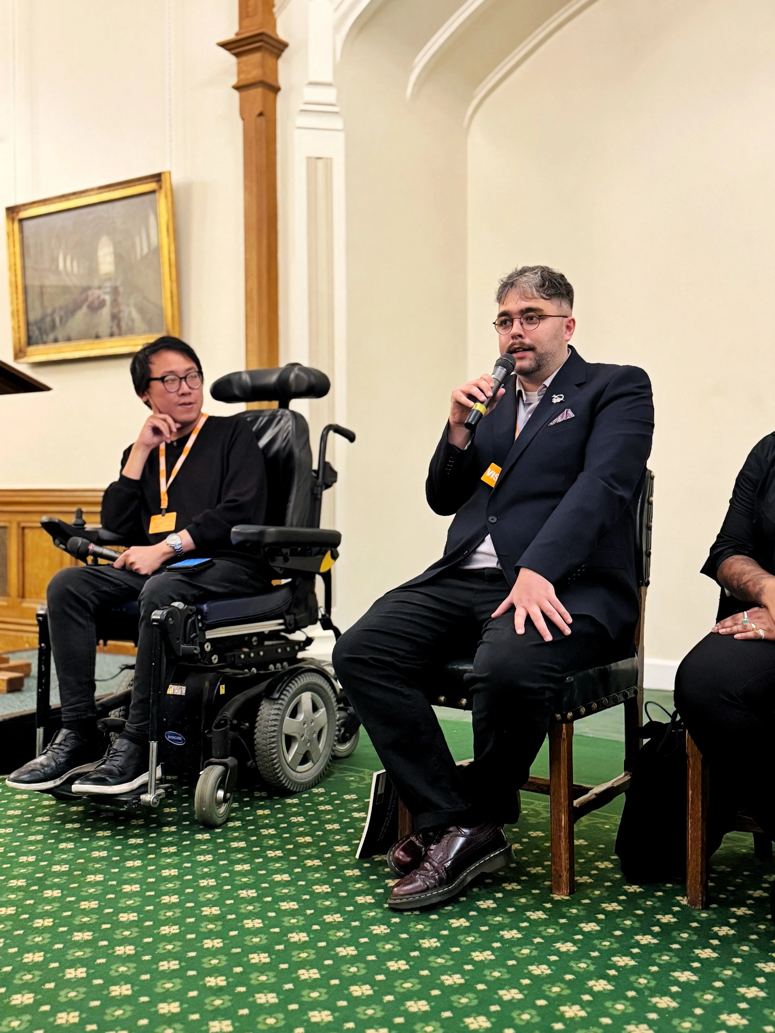 Panel discussion in the Churchill Room, Houses of Parliament, with James seated in a wheelchair and Gáibhin McGranaghan speaking into a microphone, as part of the Disability Policy Centre event.