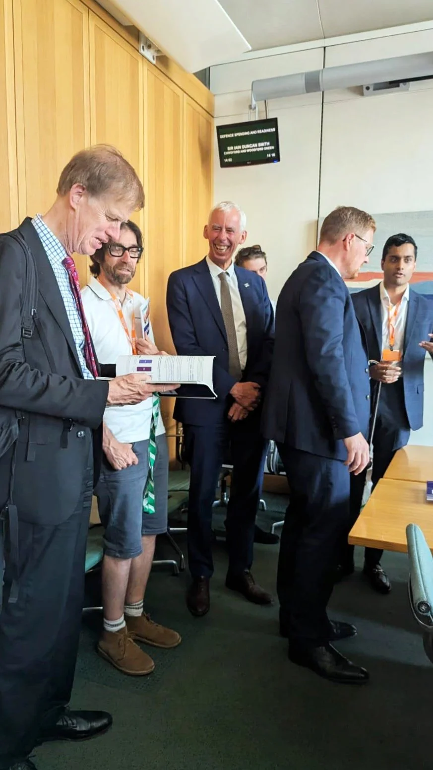 Sir Stephen Timms reads the Disability Policy Centre’s Access to Work report while John Milne MP stands beside him, with Arun from DPC speaking to attendees during the parliamentary drop-in event.