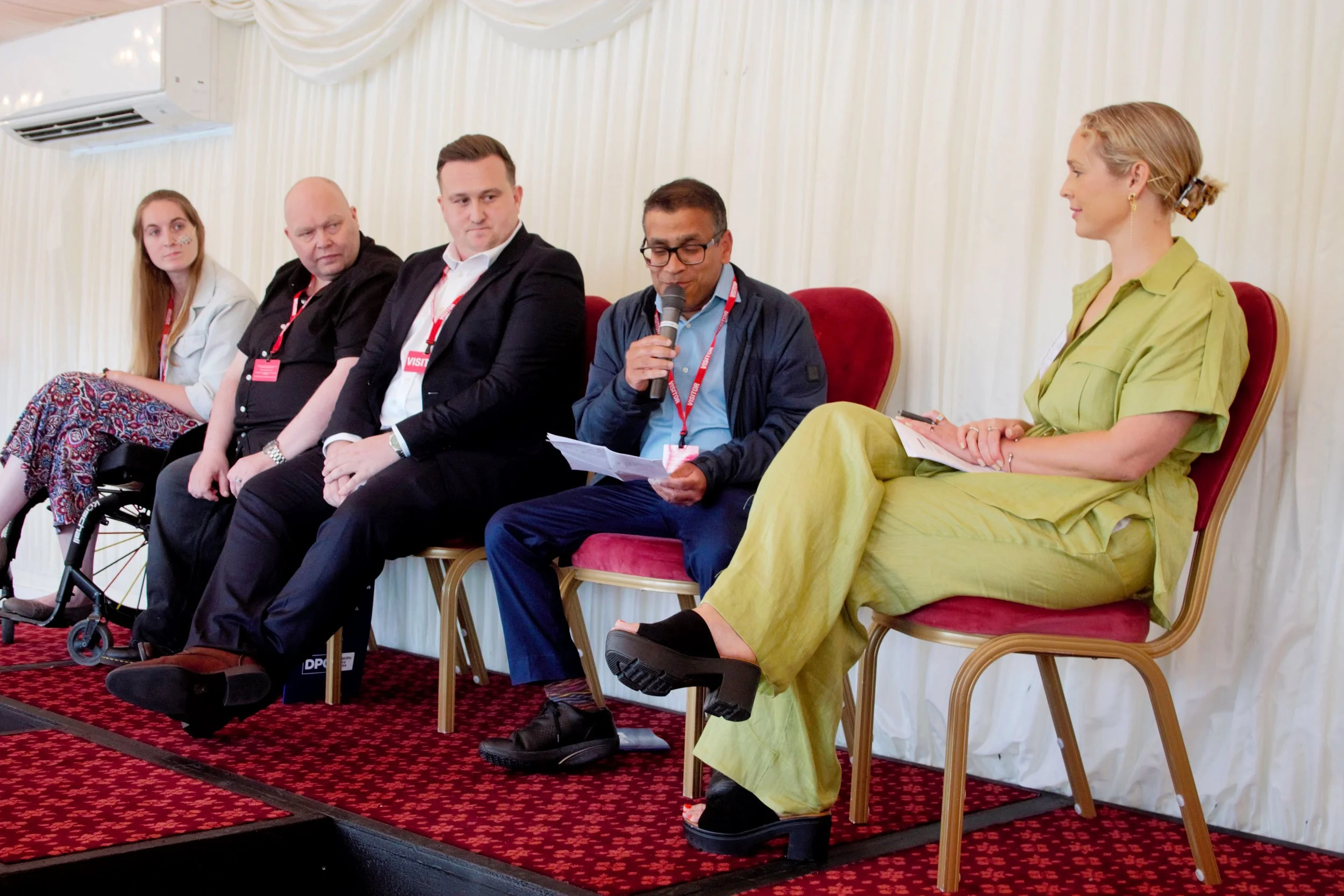 Photograph of seated panel on the stage of guest speakers, starting from far right Charli Skinner, Dr Kush Kanodia, Daniel Cook, Matt Lloyd PLY and Mary FitzMeilton. Dr Kush Kanodia is holding a piece of paper and speaking with the microphone