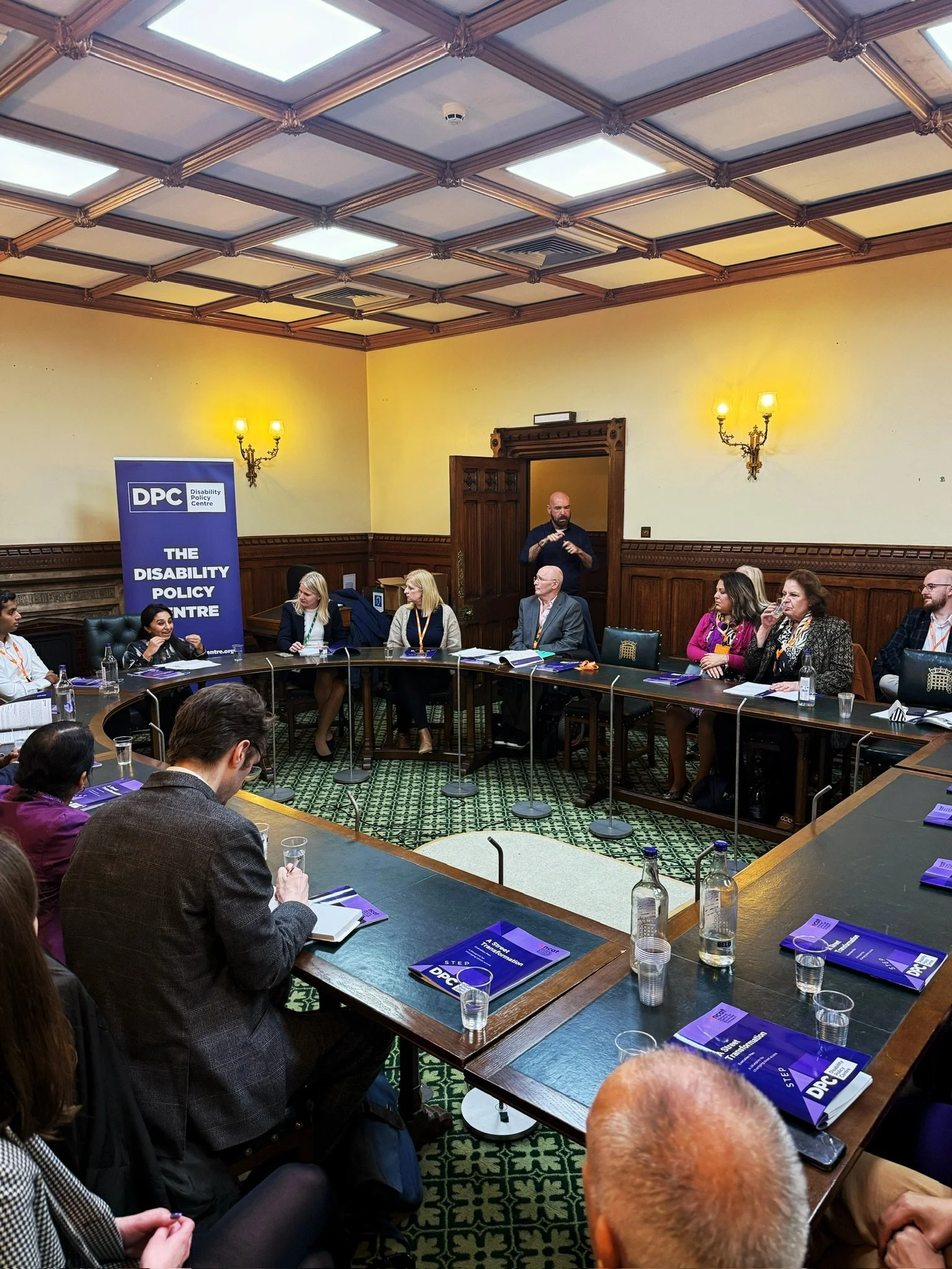 Panel discussion in a parliamentary room hosted by the Disability Policy Centre. At the front, from left to right: Dr Shani Dhanda (chair), Rebecca Paul MP, Louise Connop, and Ian Oakley, seated beside a DPC banner.