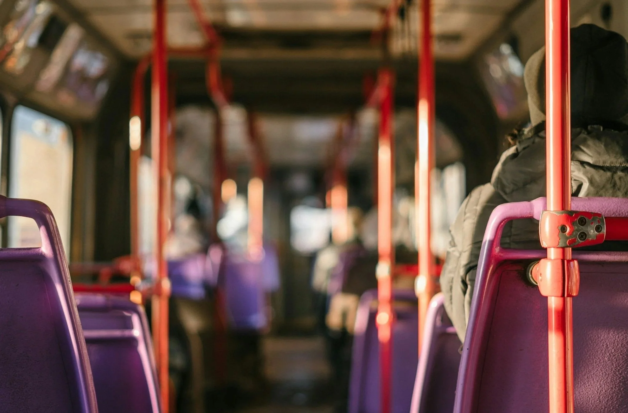 A photograph shot in the inside of a public bus. There are passengers seated in the background on purple chairs.