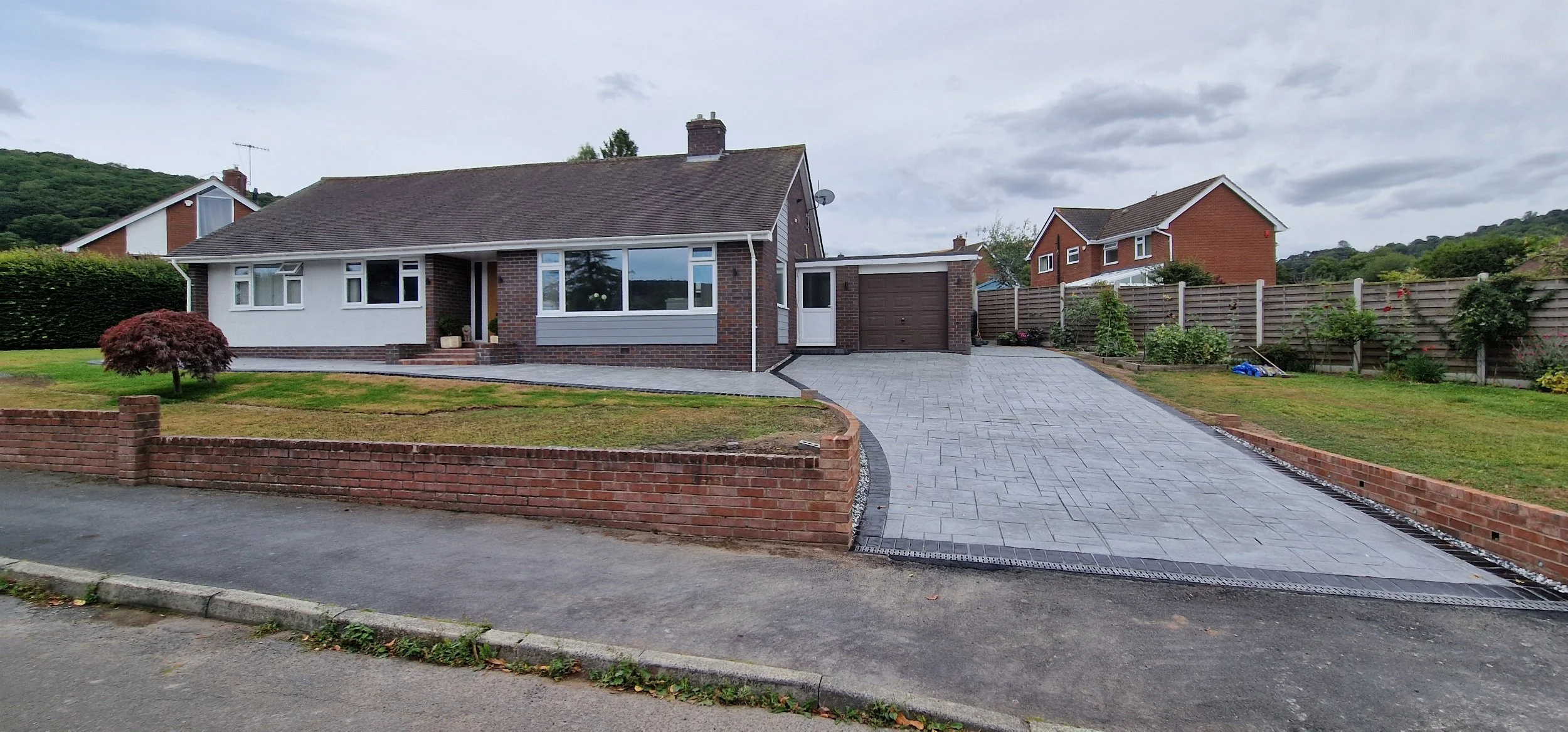 Printed concrete drive and patio in dove gray colour and Grand Ashlar print with hand stained contrasting brick soldier course border. The Driveway opening was widened and decking lights on twilight sensor installed to provide ambience during low lig