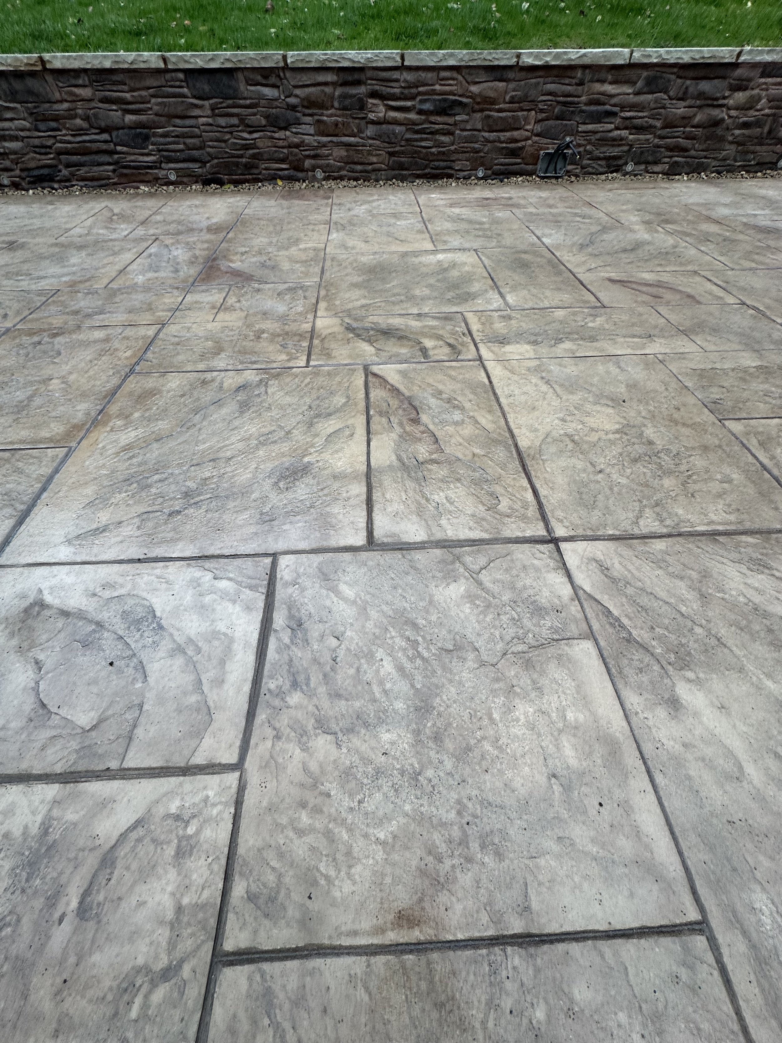 Extra large Ashlar Slate printed concrete in biscuit with charcoal release agent and a wallcrete rendered retaining wall printed in Mountain Dry Stack and hand stained to give natural looking variation