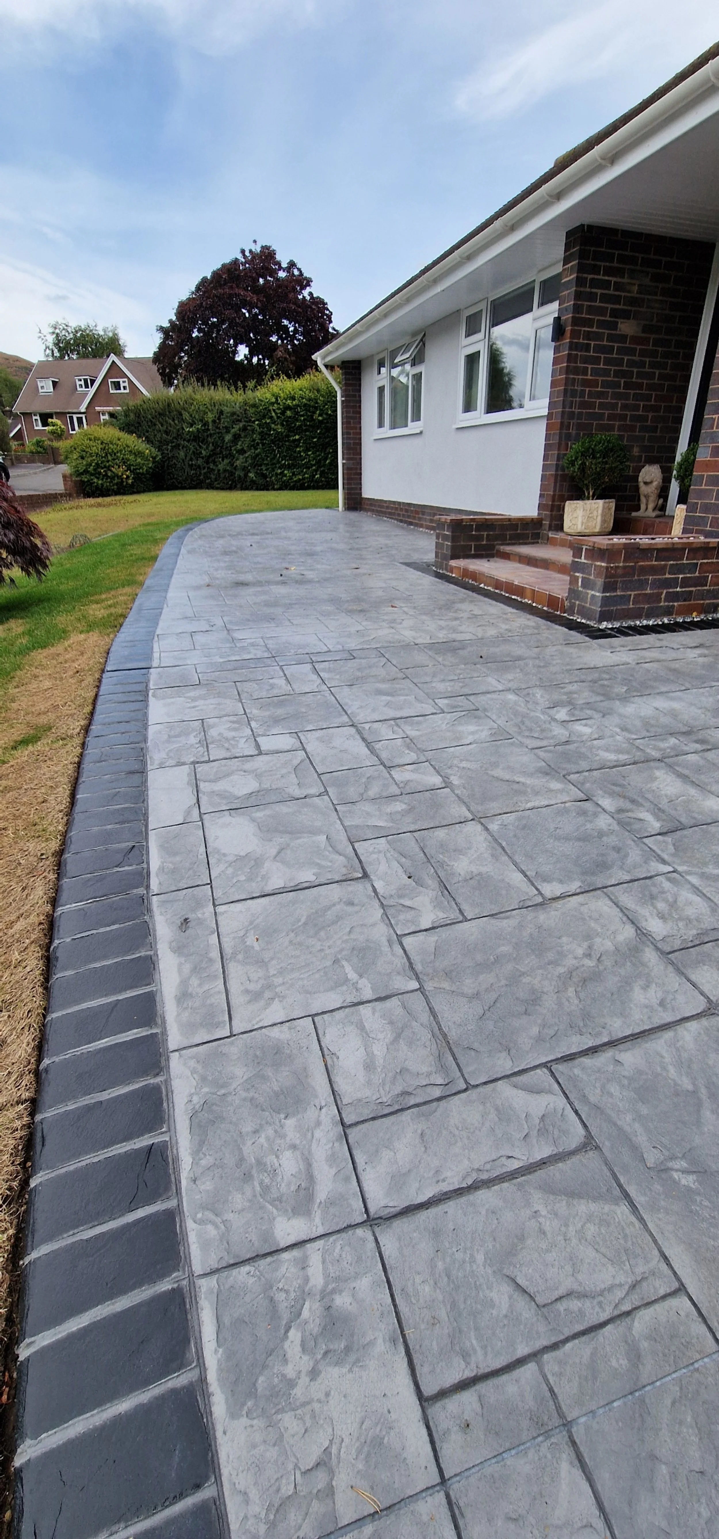 Printed concrete drive and patio in dove gray colour and Grand Ashlar print with hand stained contrasting brick soldier course border.
