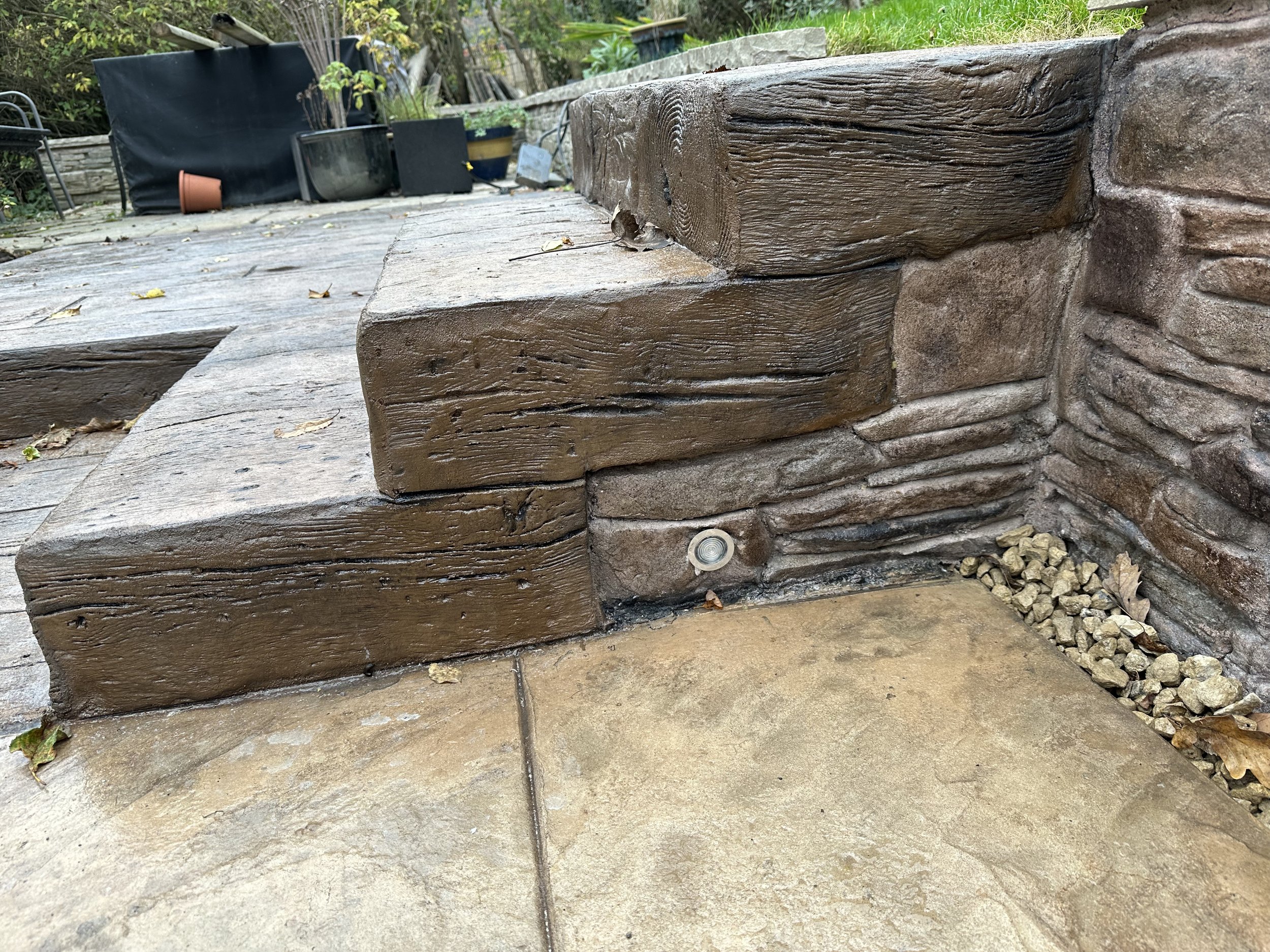 Side view of Timber printed concrete step including Decking lights and inset stone effect render in continuation with the wall