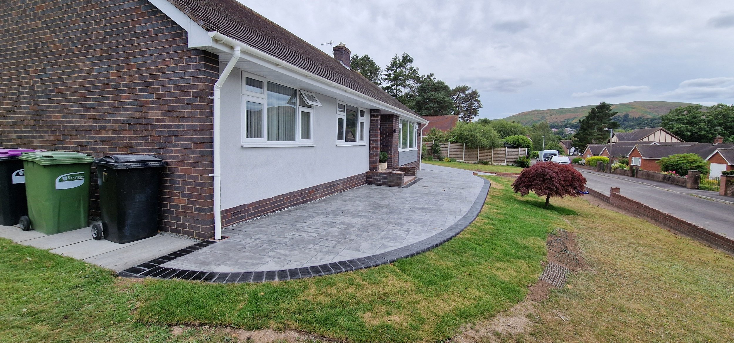 Printed concrete drive and patio in dove gray colour and Grand Ashlar print with hand stained contrasting brick soldier course border.