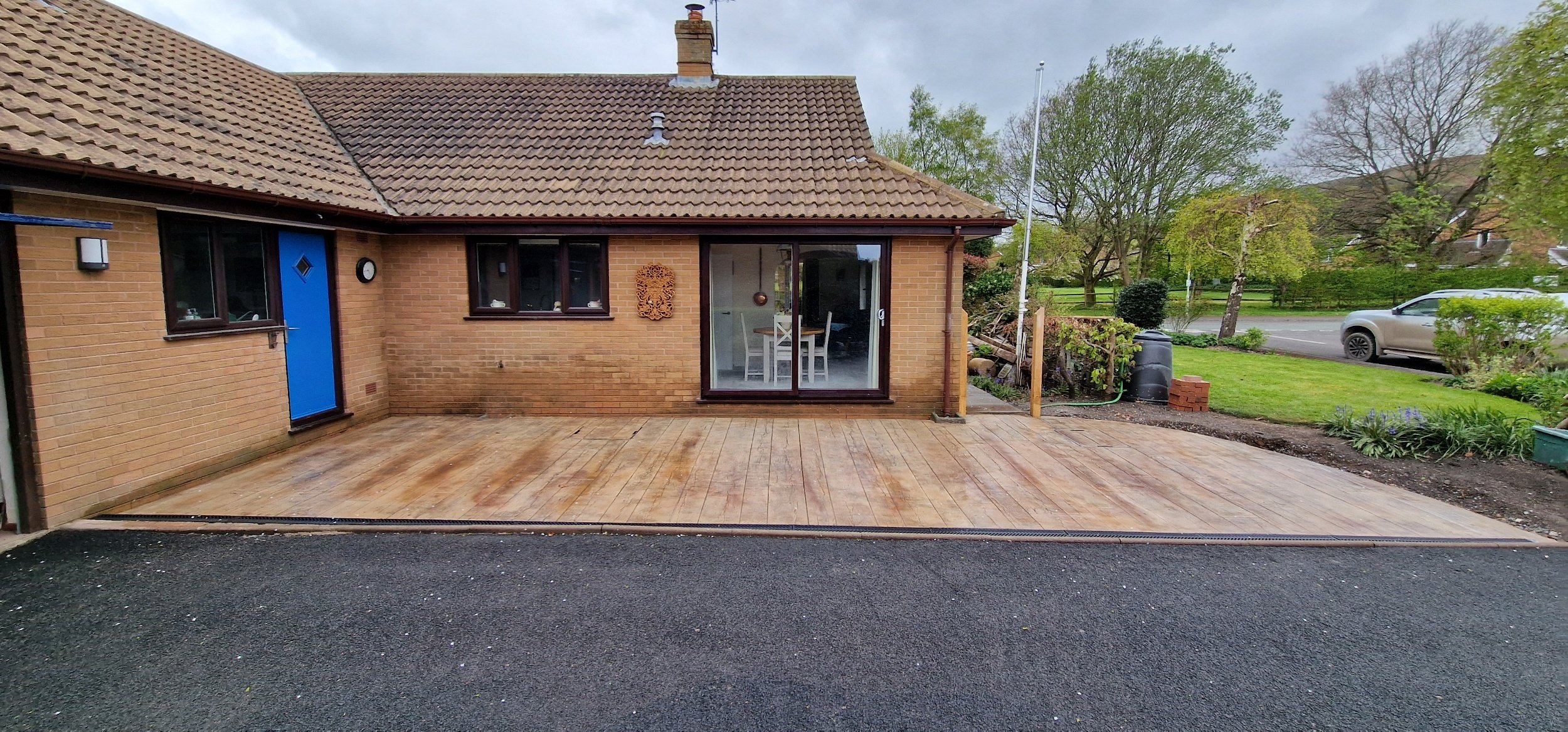 Reclaimed Timber printed concrete in biscuit. Linear drains leading to soak away make this Project SUDS compliant and a later addition of a low wall rendered in wallcrete and printed on all aspects to resemble timber and a lich gate were added