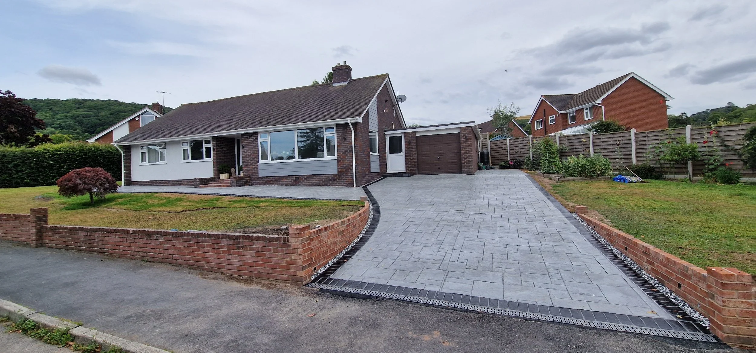 Printed concrete drive and patio in dove gray colour and Grand Ashlar print with hand stained contrasting brick soldier course border. The Driveway opening was widened and decking lights on twilight sensor installed to provide ambience during low lig