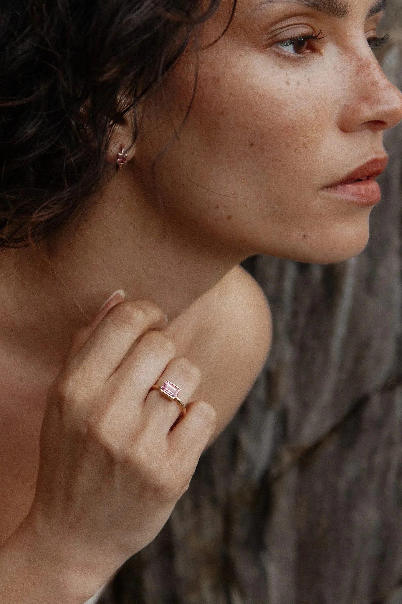Vue rapprochée du visage d'une femme, portant une bague avec une pierre rose devant un fond flou.