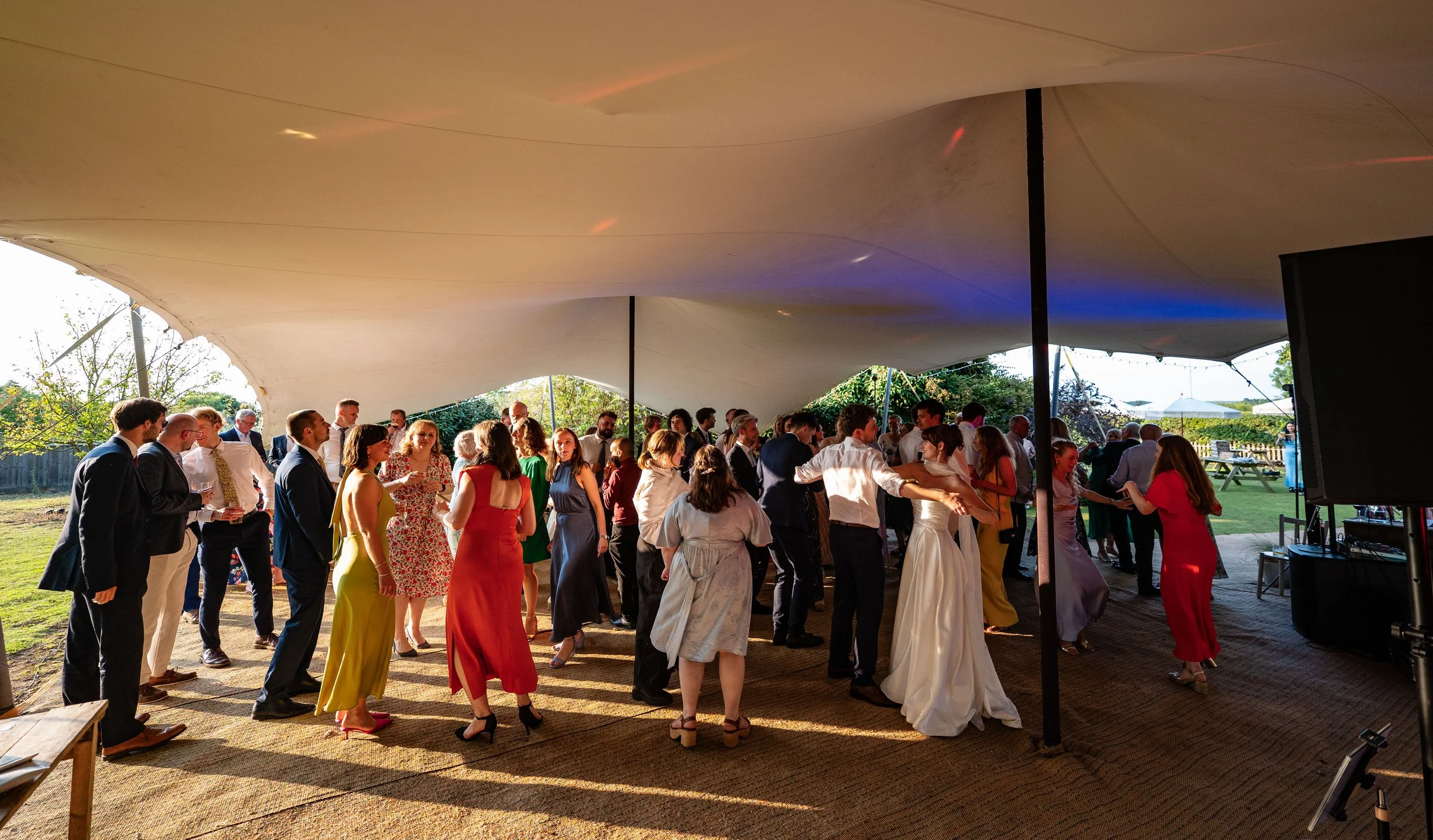 People dancing and socializing at an outdoor wedding reception under a large canopy on a sunny day.
