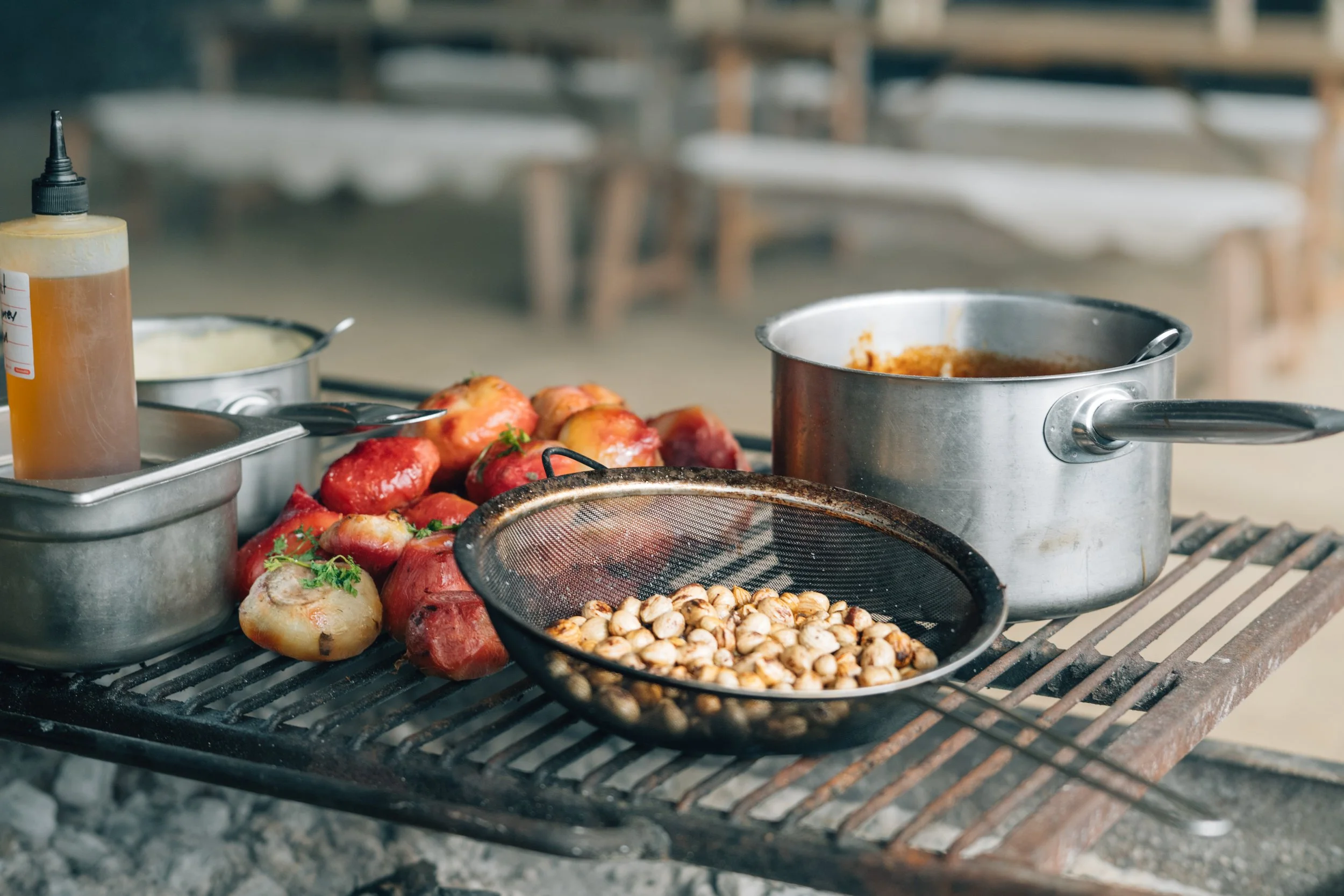 Food preparation setup with apples, onions, a bottle of sauce, a pot of curry, and a bowl of chickpeas on a grill outdoors.
