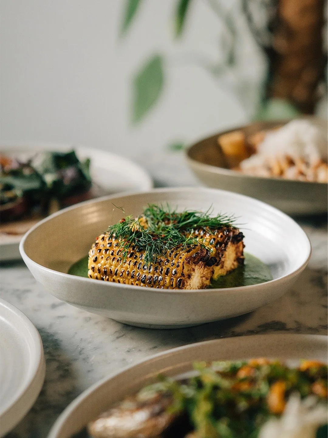 Locally grown by our friends at @flourishproduce and charred to perfection over the wood-fired hearth, this isn’t just any corn. Brushed with dill butter, scattered with Aleppo pepper, and served in a pool of vibrant herb sauce, it’s the