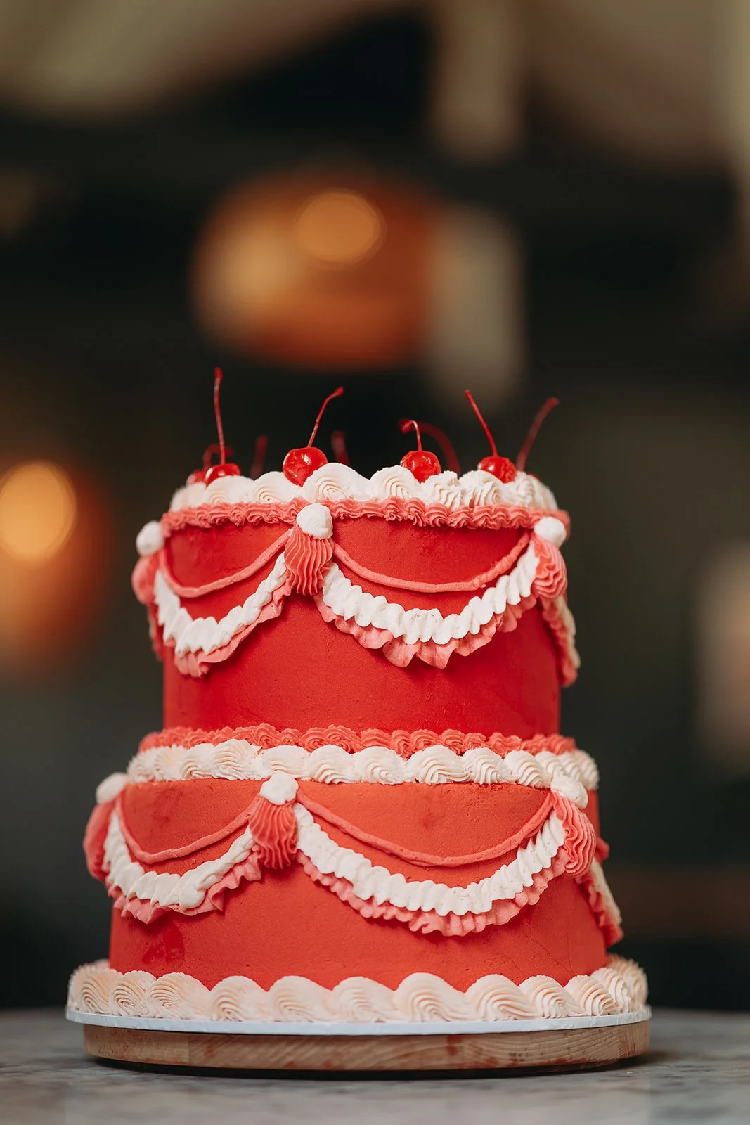 A three-tier red and white decorated birthday cake with cherries on top.