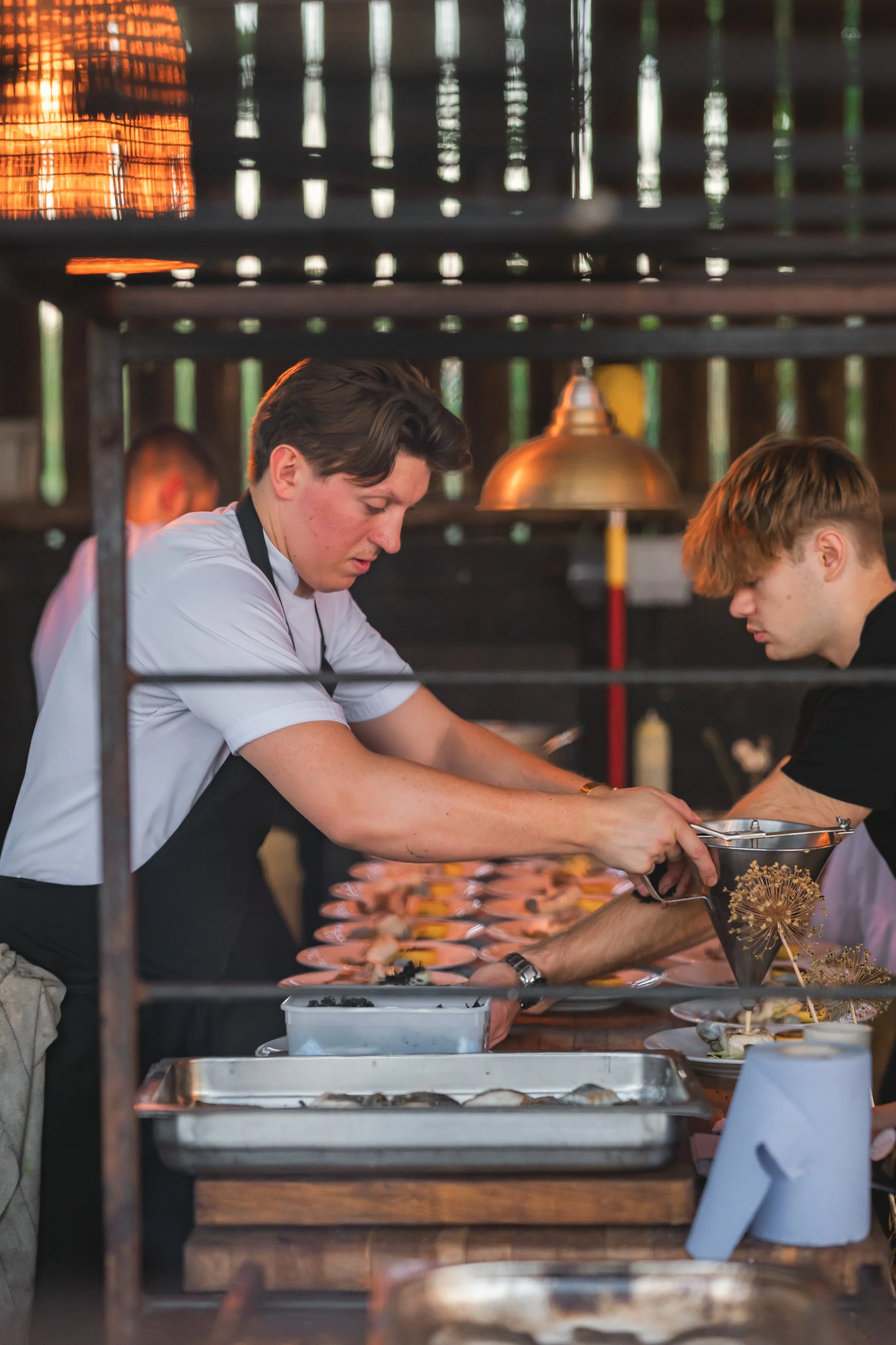 Two chefs working together in a kitchen preparing dishes, with various kitchen tools and ingredients on the counter.